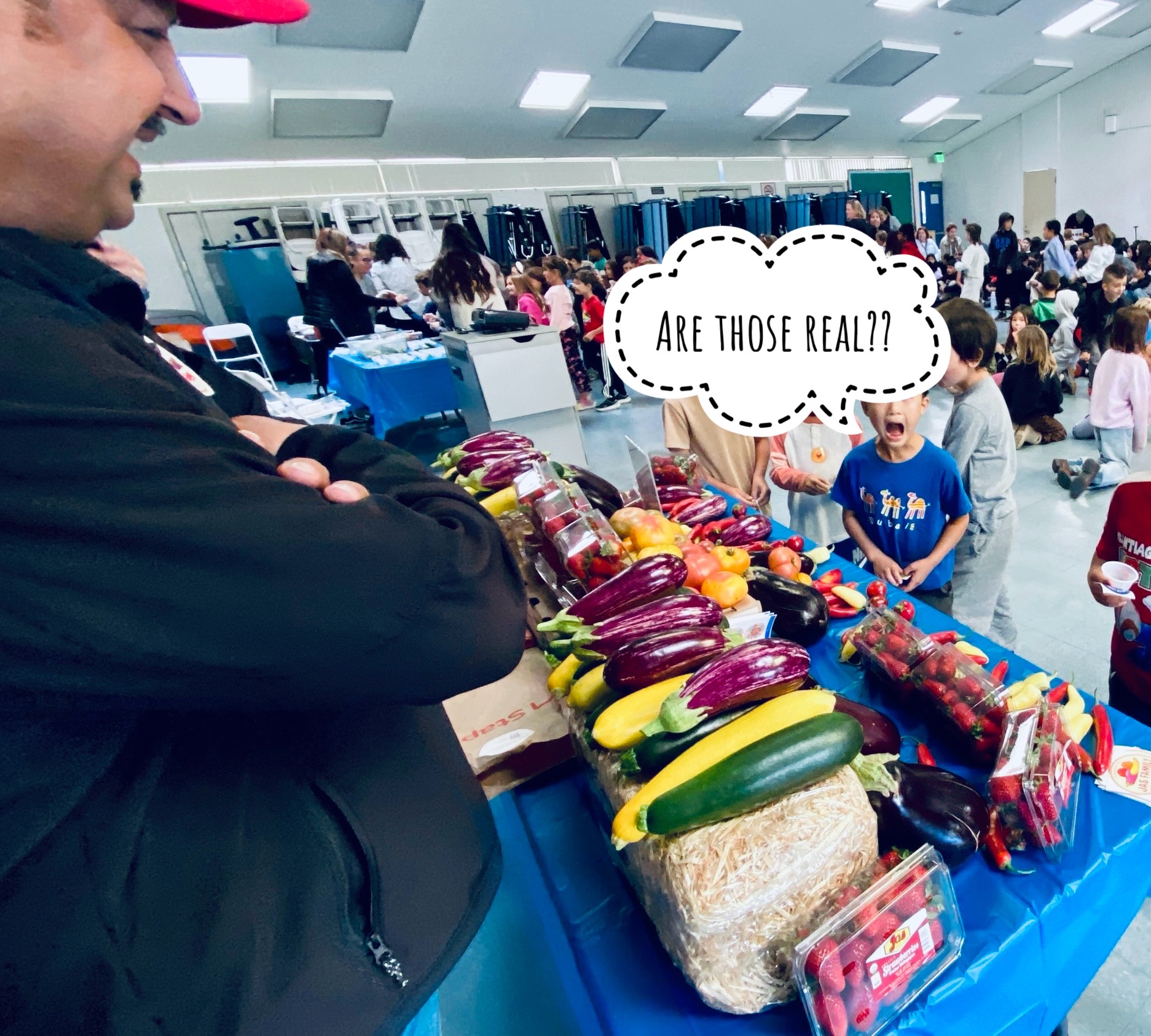 A young student expresses surprise at the colorful produce on the table while Farmer Tony smiles
