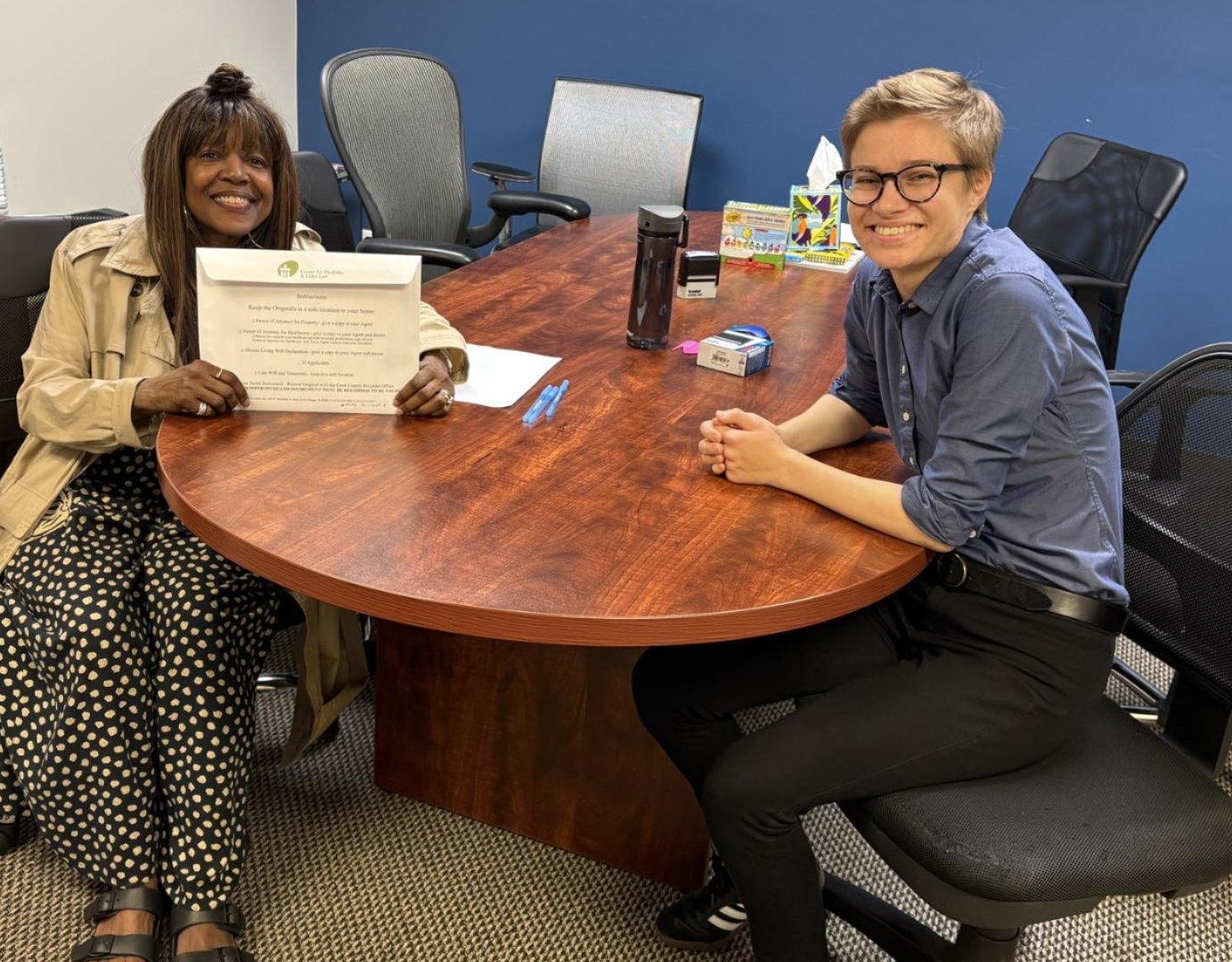 CDEL client with CDEL staff attorney Kate Milvert holding up completed estate planning documents at CDEL’s office