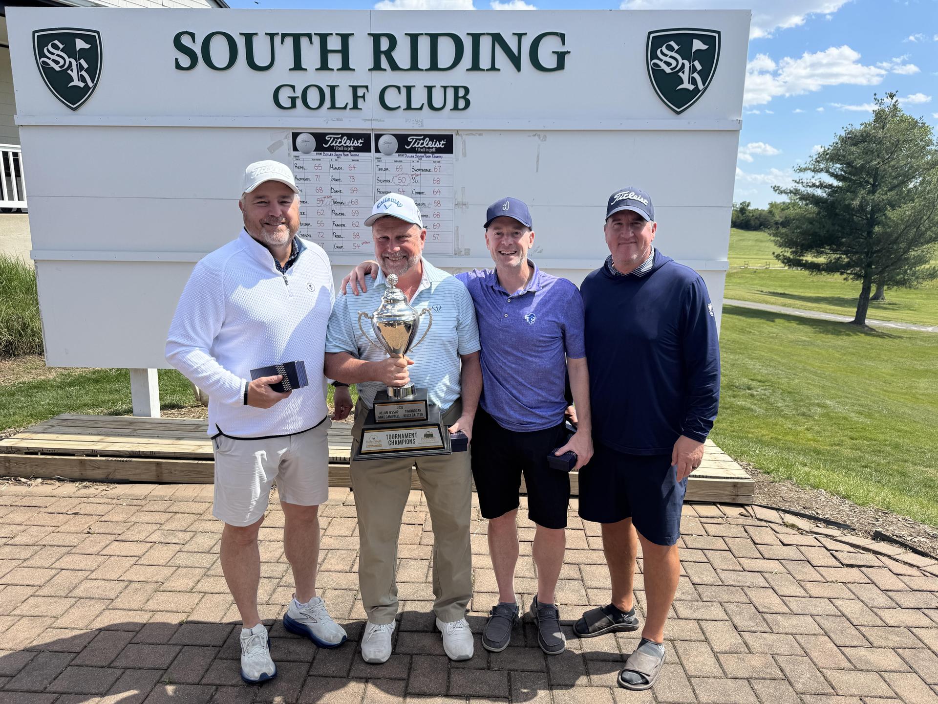 Four men standing posing with trophy in front of South Riding Golf Club sign outside