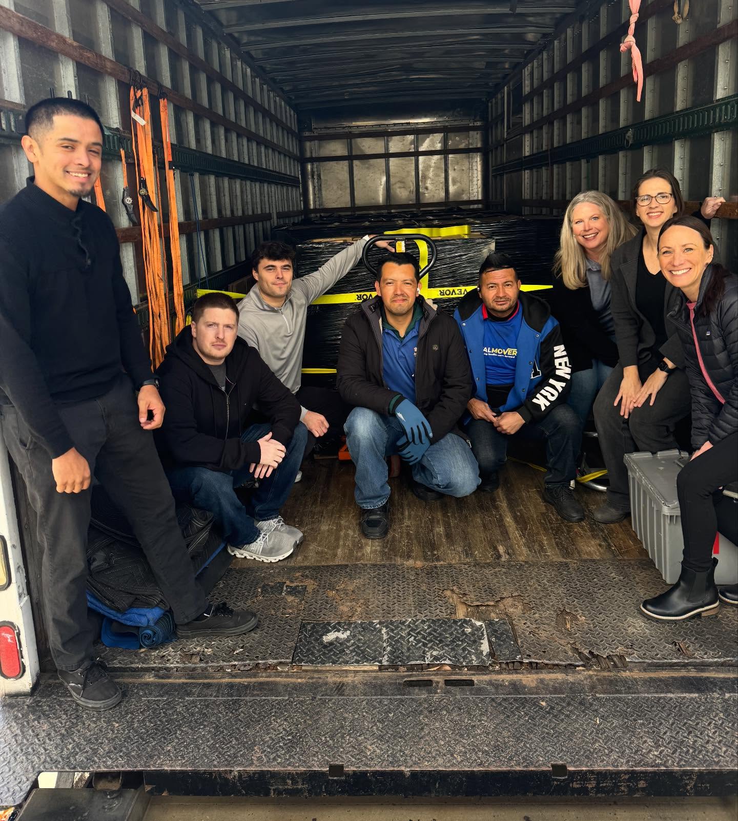 Group of people posing for picture inside the moving truck filled with pallets of food boxes