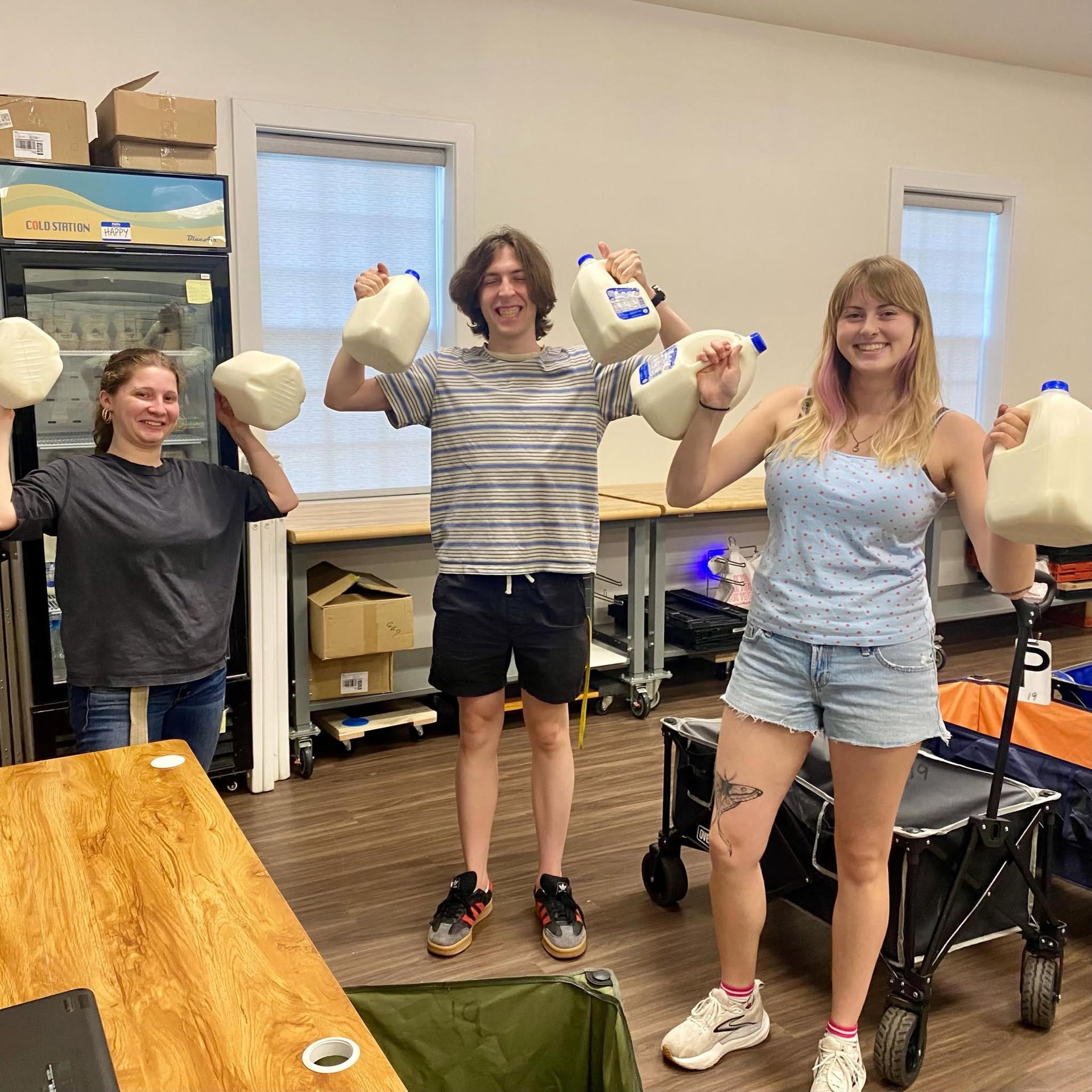 Three college student volunteers holding gallons of milk at the Pantry