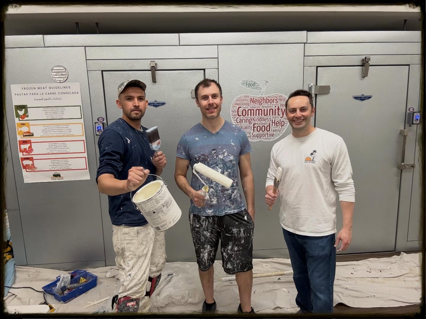 Three men standing in front of Pantry freezer door holding paint roller, paint brush and can of paint