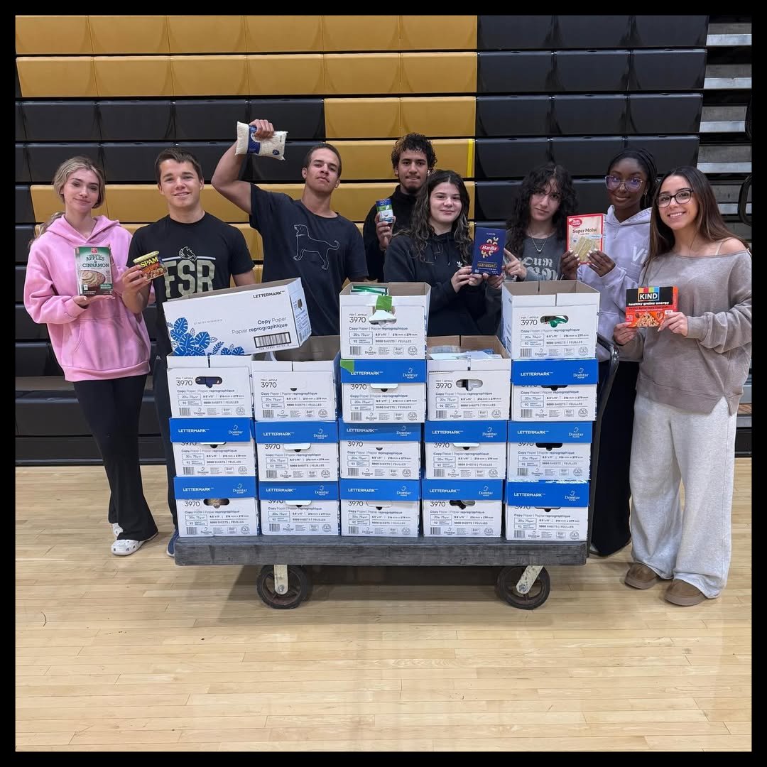 Students standing behind cart of food donations in white boxes