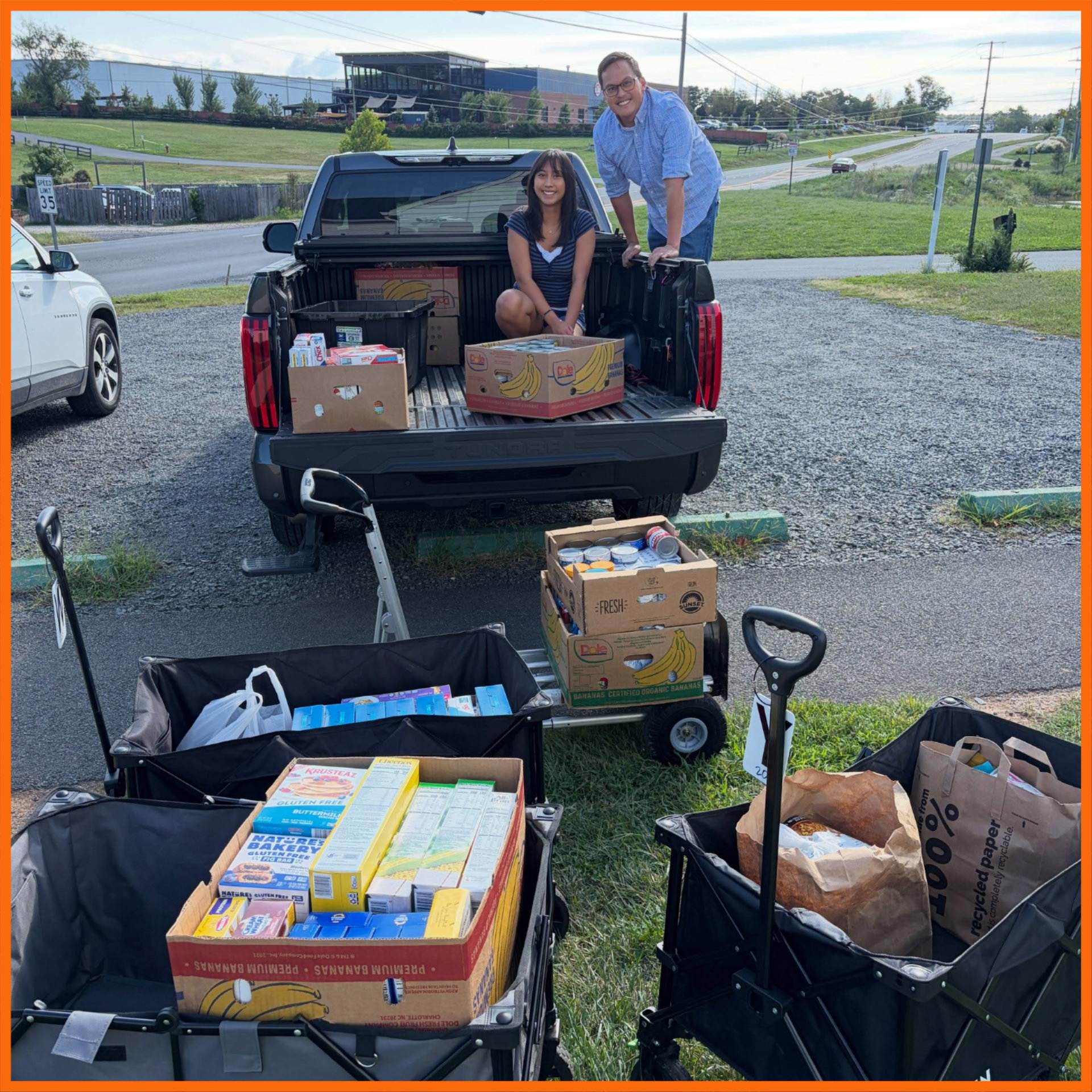 picture outside of two people in back of pick-up truck with donation boxes and wagons loaded with donations