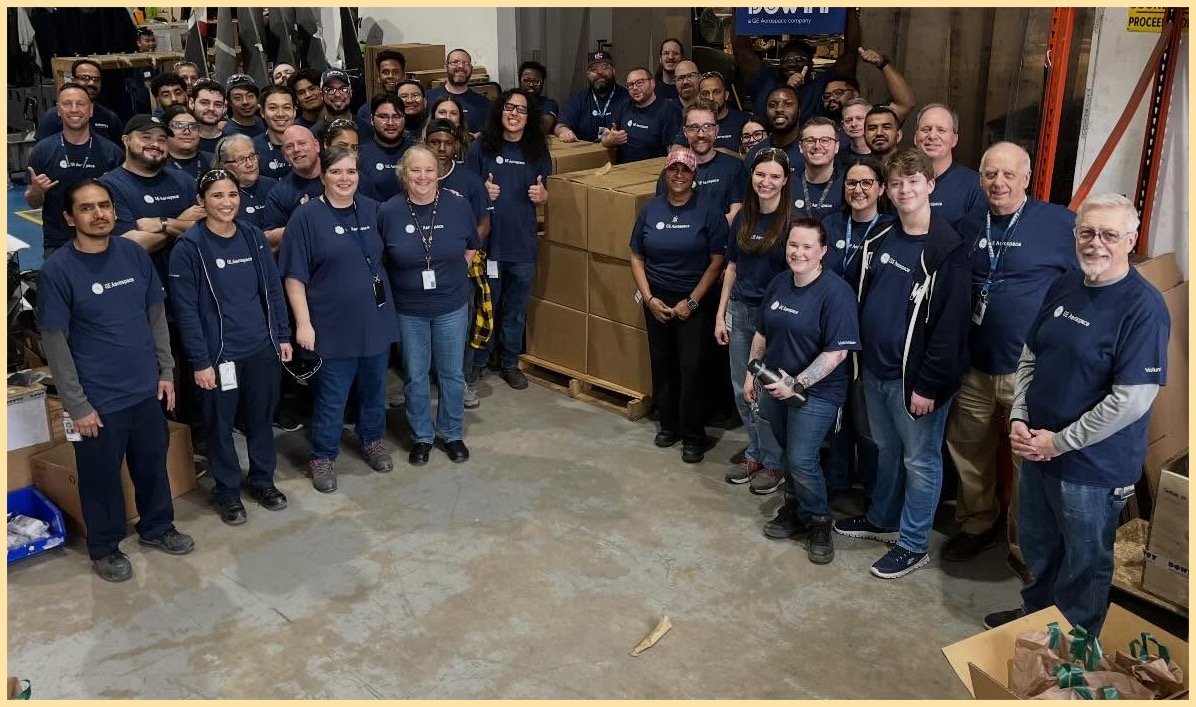 GE Aerospace employees standing in group photo wearing blue shirts surrounded by boxes