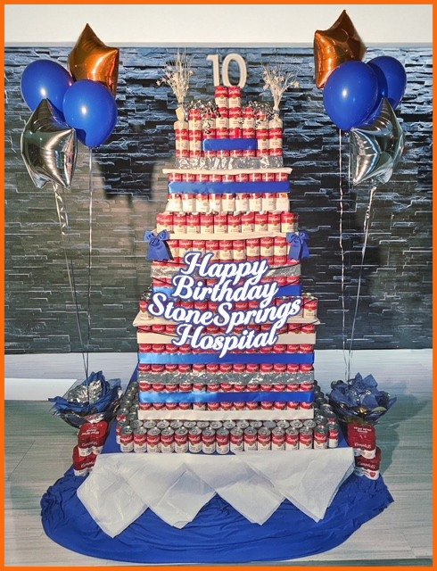 Tower of soup cans in the shape of a tiered cake with Happy Birthday sign and balloons