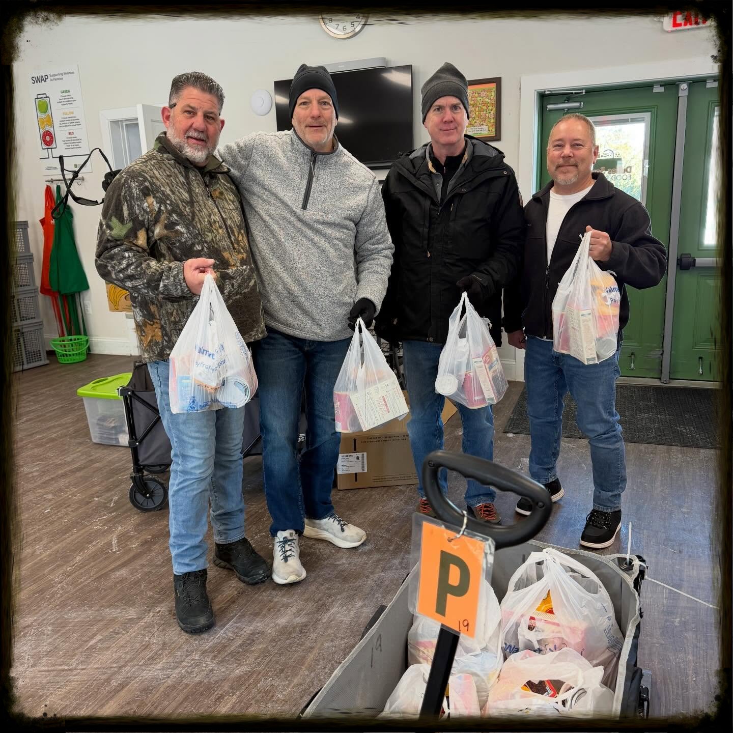 People standing behind behind wagon of food holding up bags of chili meal kits