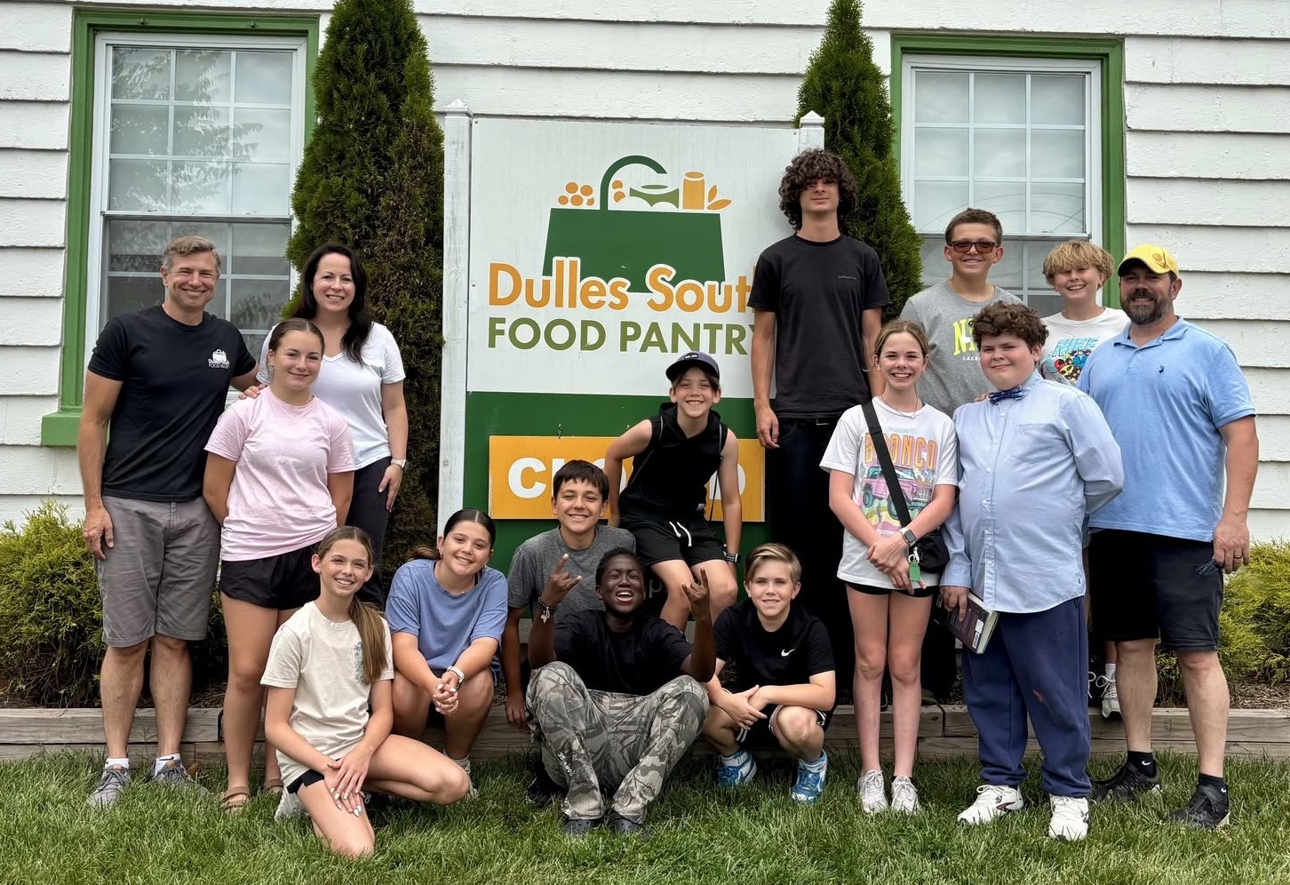 Group of adults and children standing next to Pantry sign outside