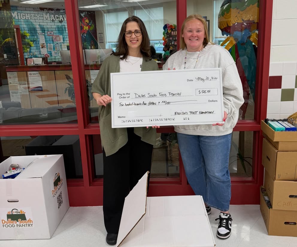 Two women posing in front of food donations holding a large ceremonial donation check