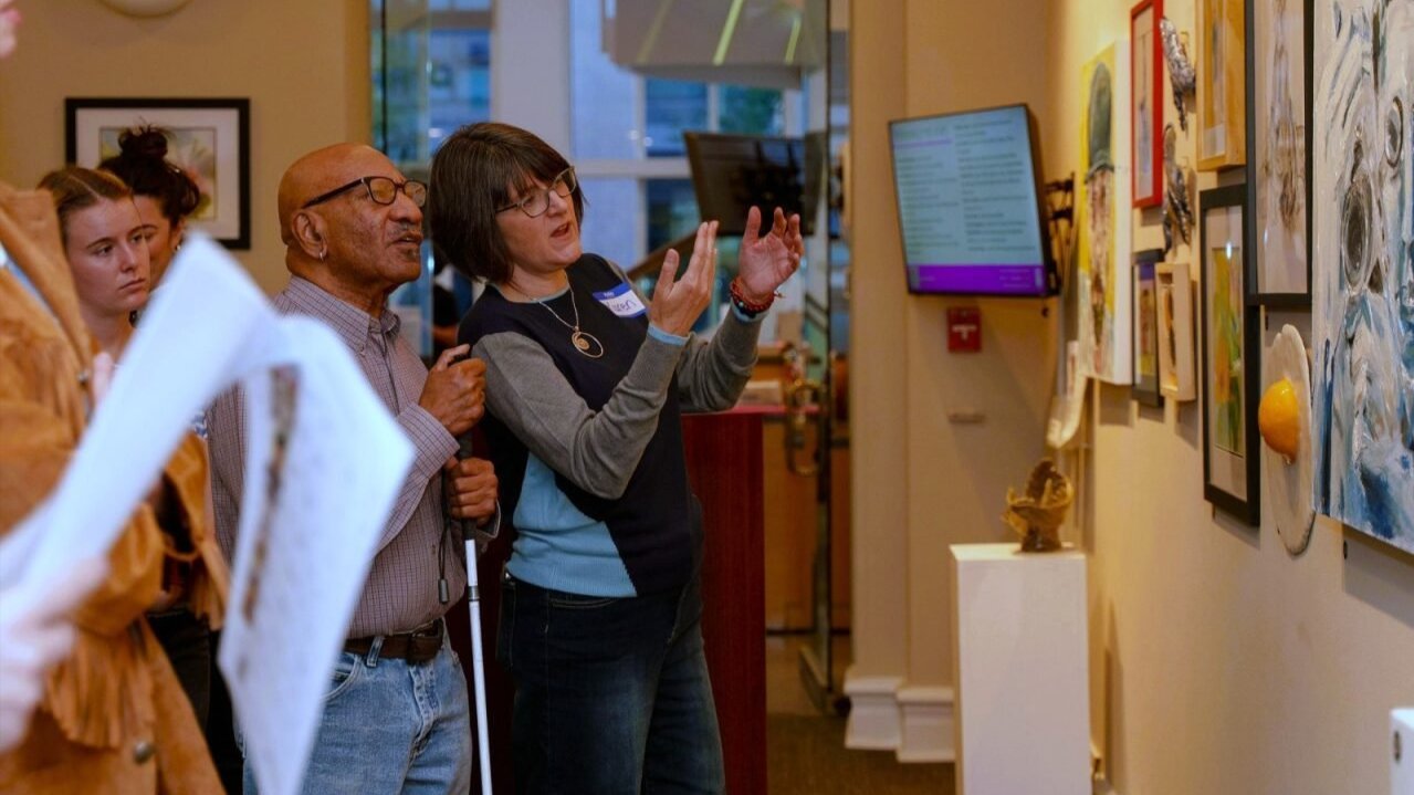 Third Friday reception featuring two individuals, one is audio describing artwork to another. Photo by Jen Scheib/