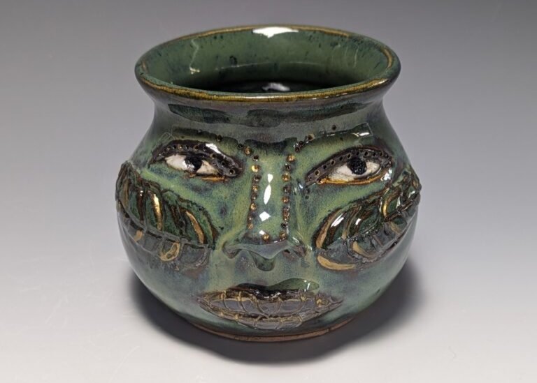 Ceramic face pot with a green glaze.