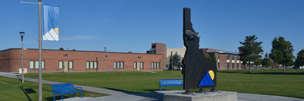 College of Eastern Idaho campus with a metal Idaho-shaped sculpture on a circular walkway, green lawn, and brick buildings.