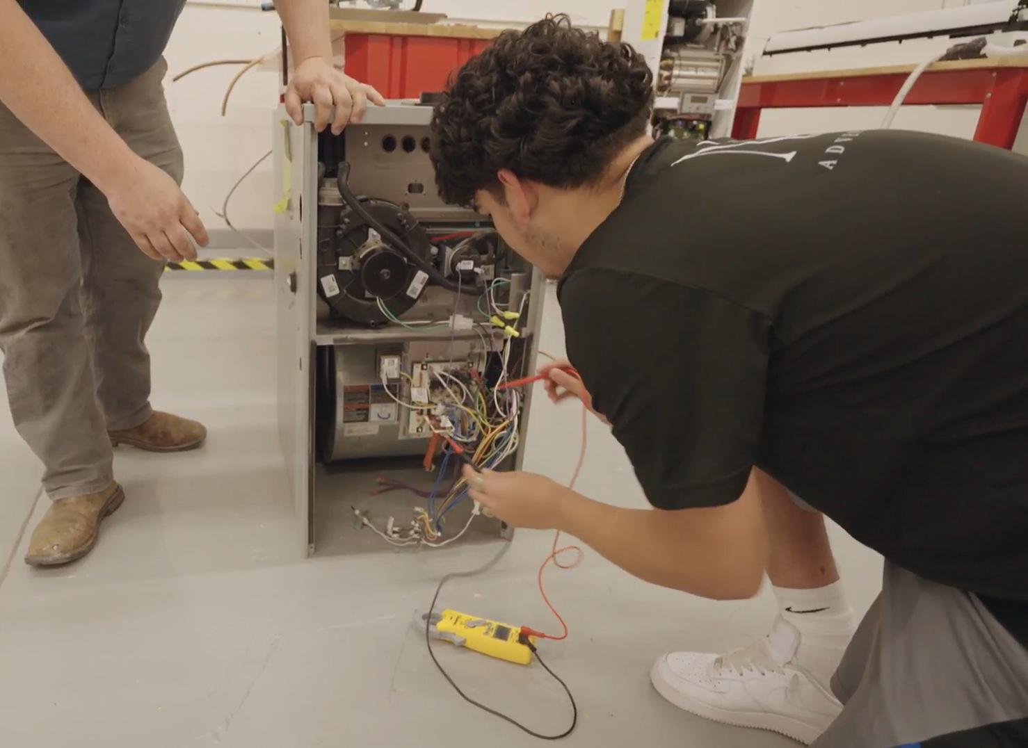 A person in an apprenticeship class at CEI works on the wiring inside an open HVAC unit.