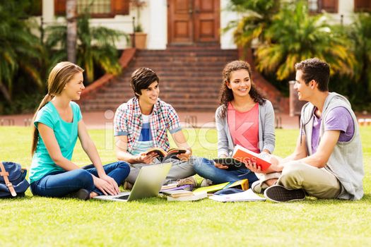 College students sitting on a lawn with laptops and textbooks