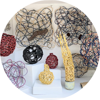 Woven abstract sculptures in various colors and shapes displayed on white shelves.
