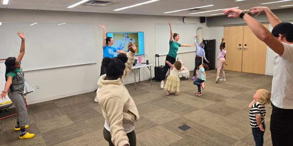 Kids of many ages practice dance moves in a room with instructors and adults.