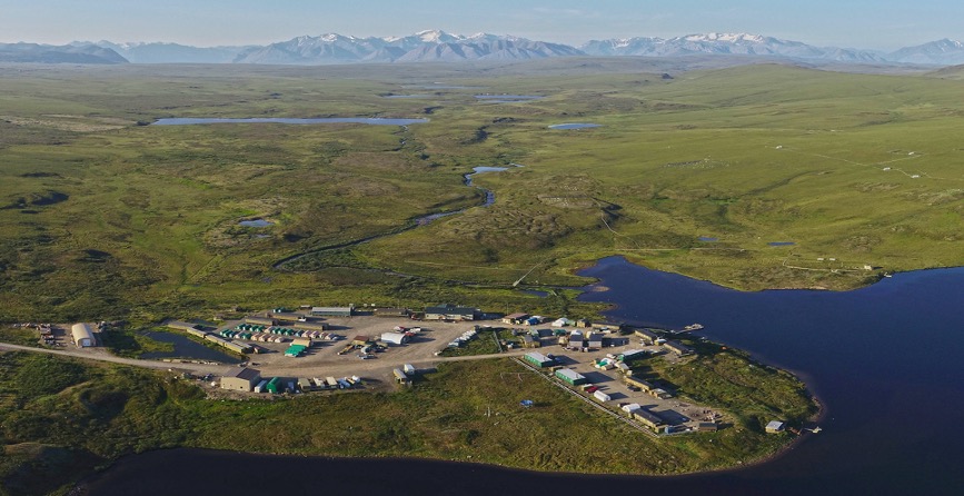 An aerial image of the Toolik Field Station. The surrounding landscape is green tundra, blue lakes and snow-capped mountains on the horizon.