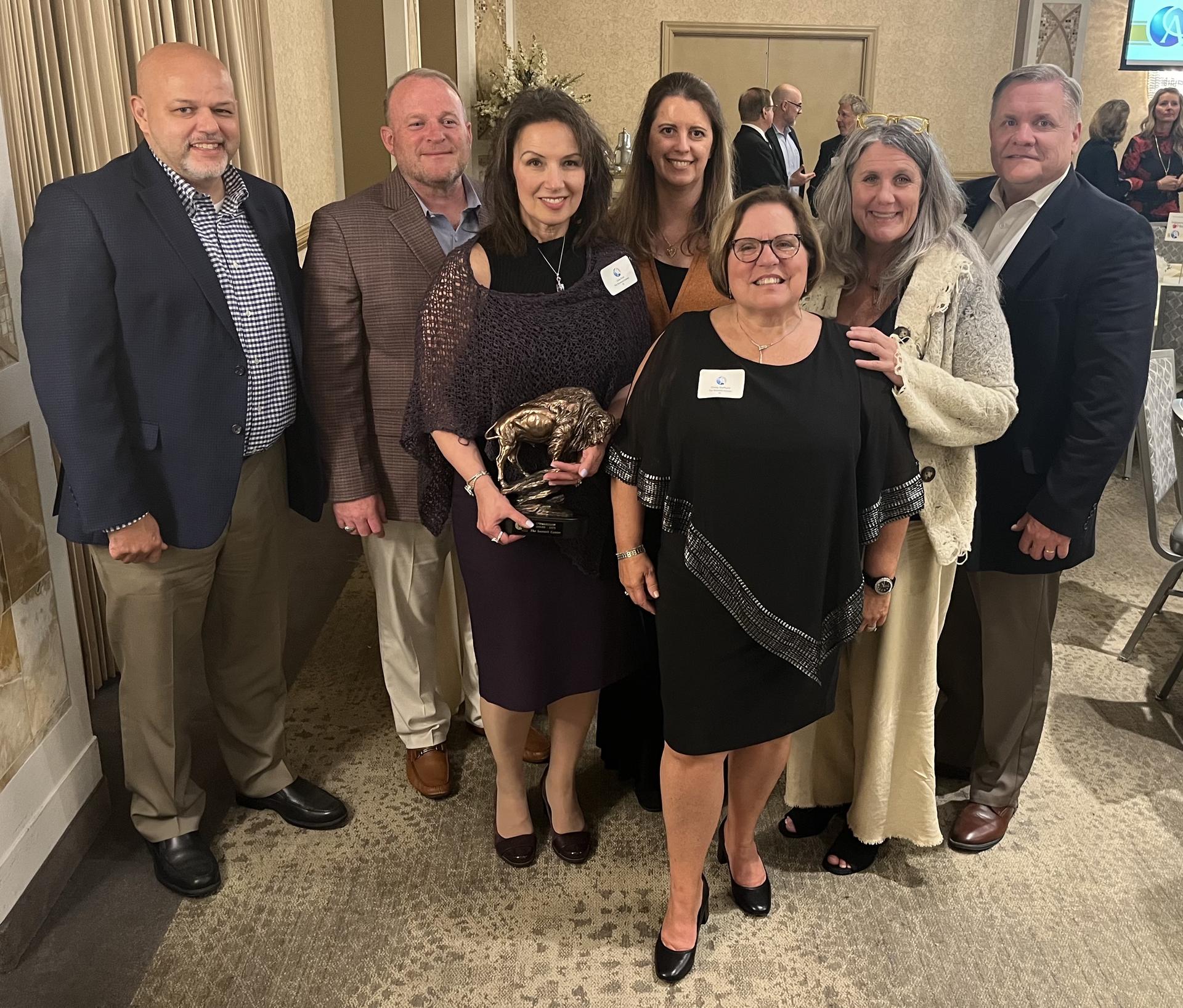 A group of people in business attire pose holding an award shaped like a Buffalo.