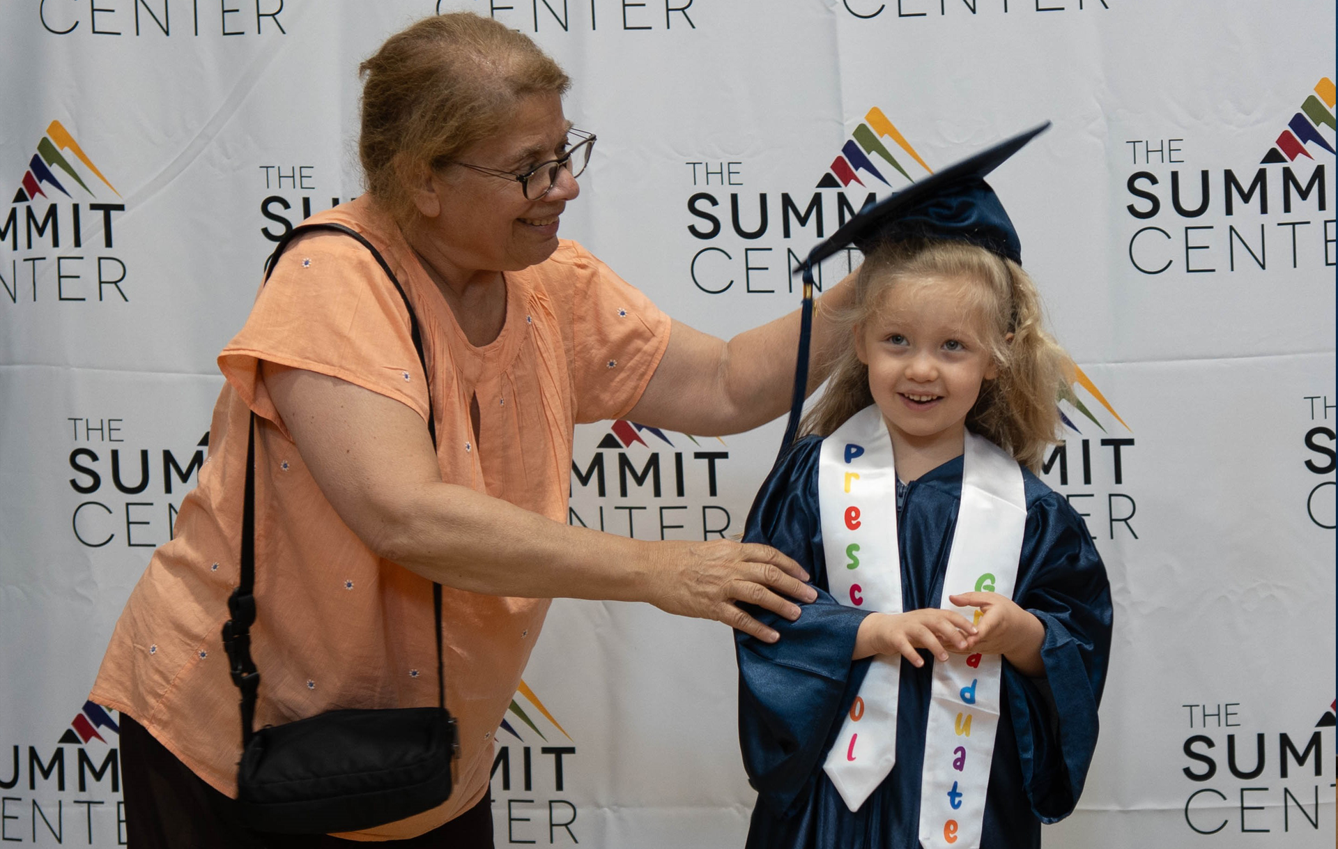 An older woman adjusts a graduation cap worn by a young girl.