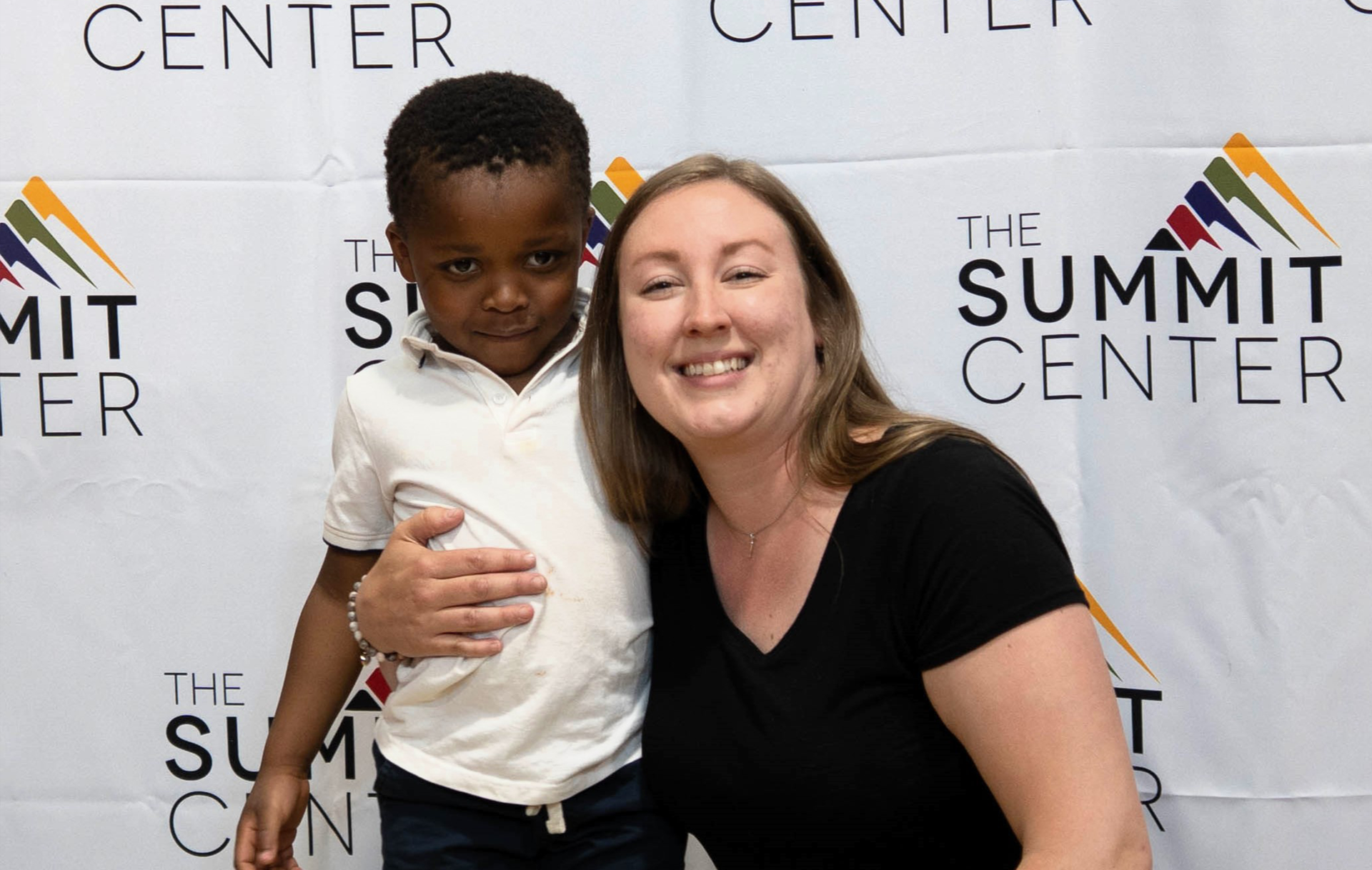 A young boy smiles as a young woman hugs him.