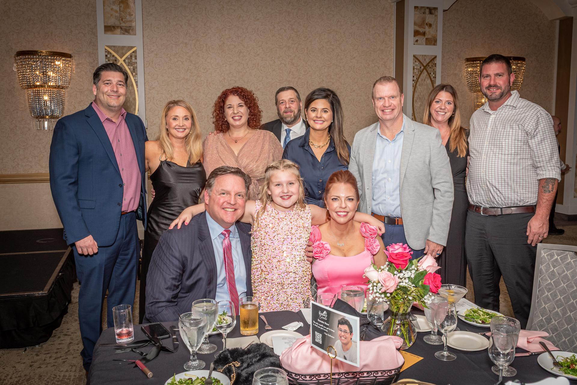 A group of elegantly dressed people gather around a table in a banquet hall.