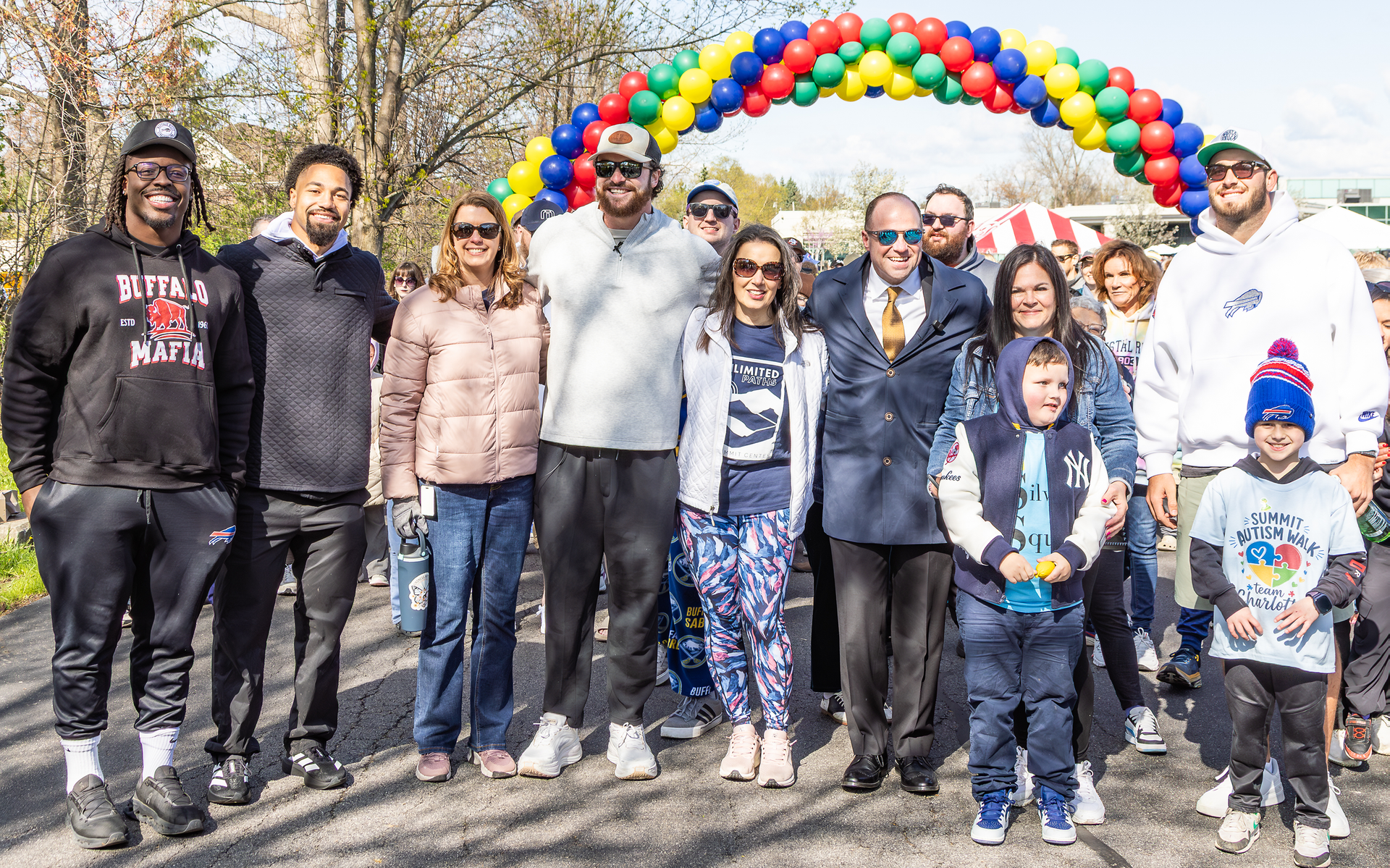 A group of people stand in front of a balloon arch outside.