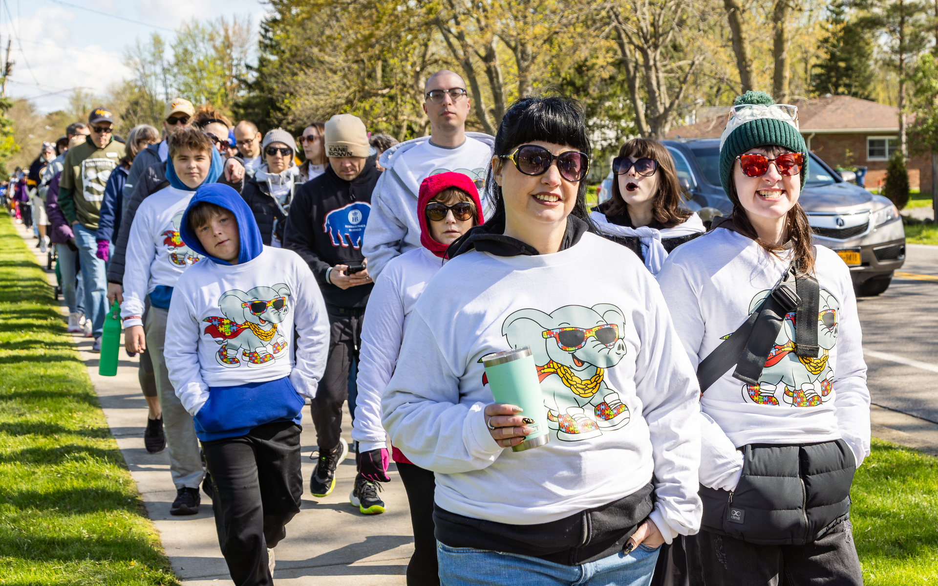 A group of people in white sweatshirts walk down the sidewalk.