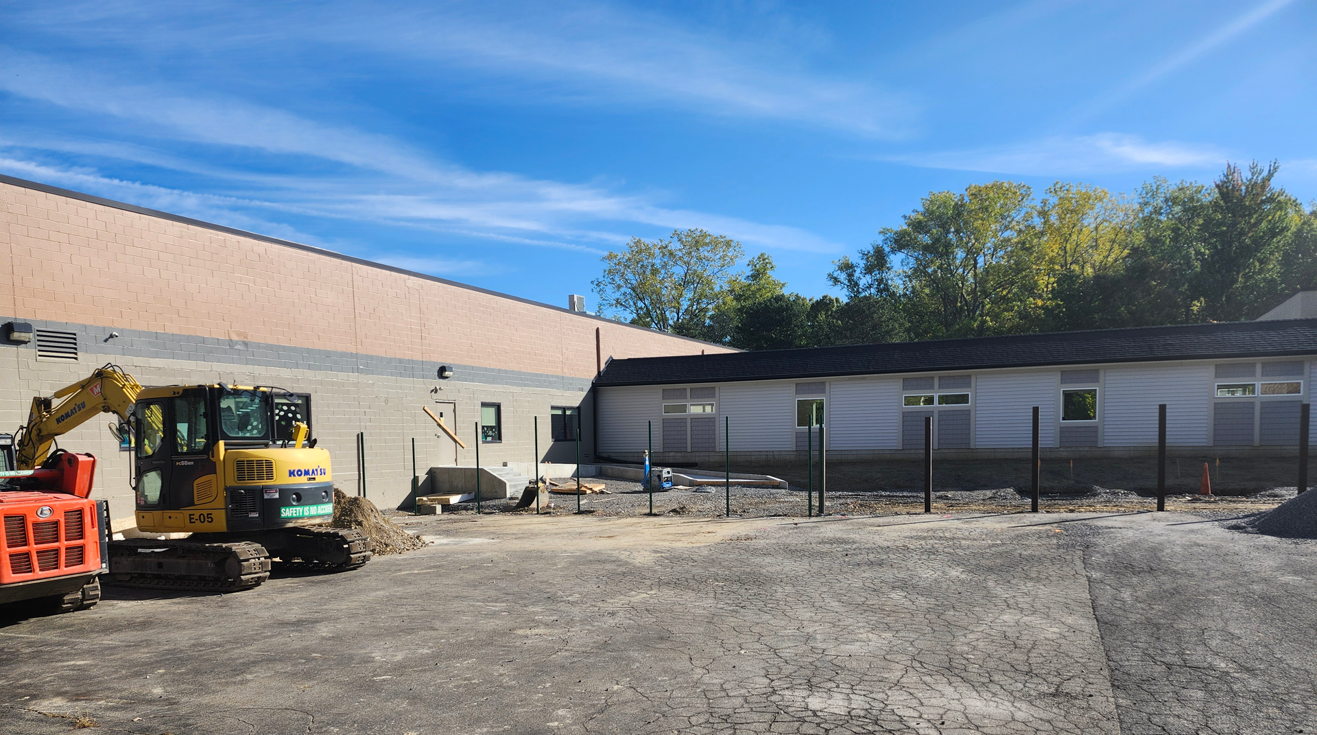 An excavator parked by a building and posts line the space where a courtyard will go.