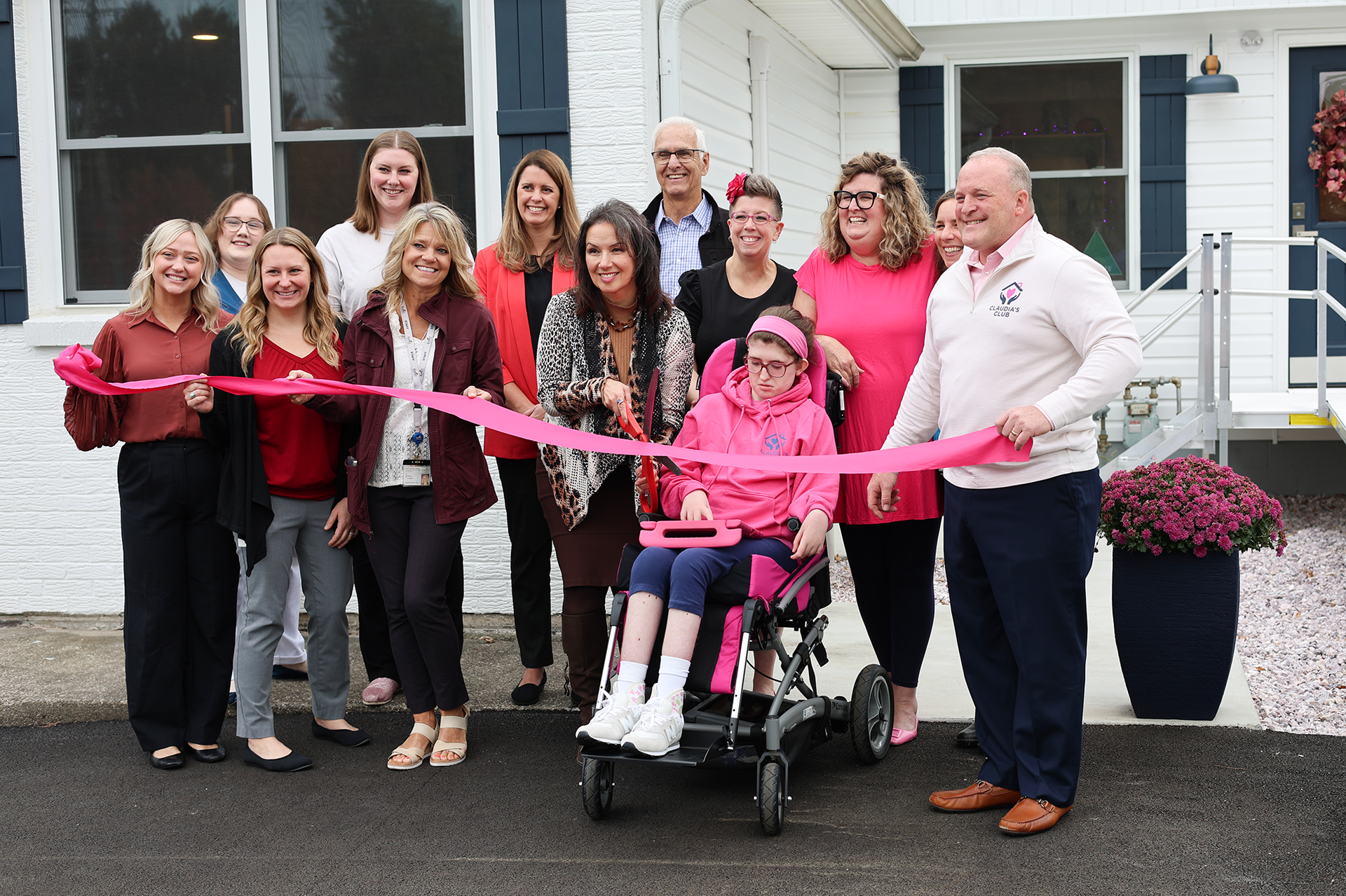A group of people outside a white house holding a pink ribbon