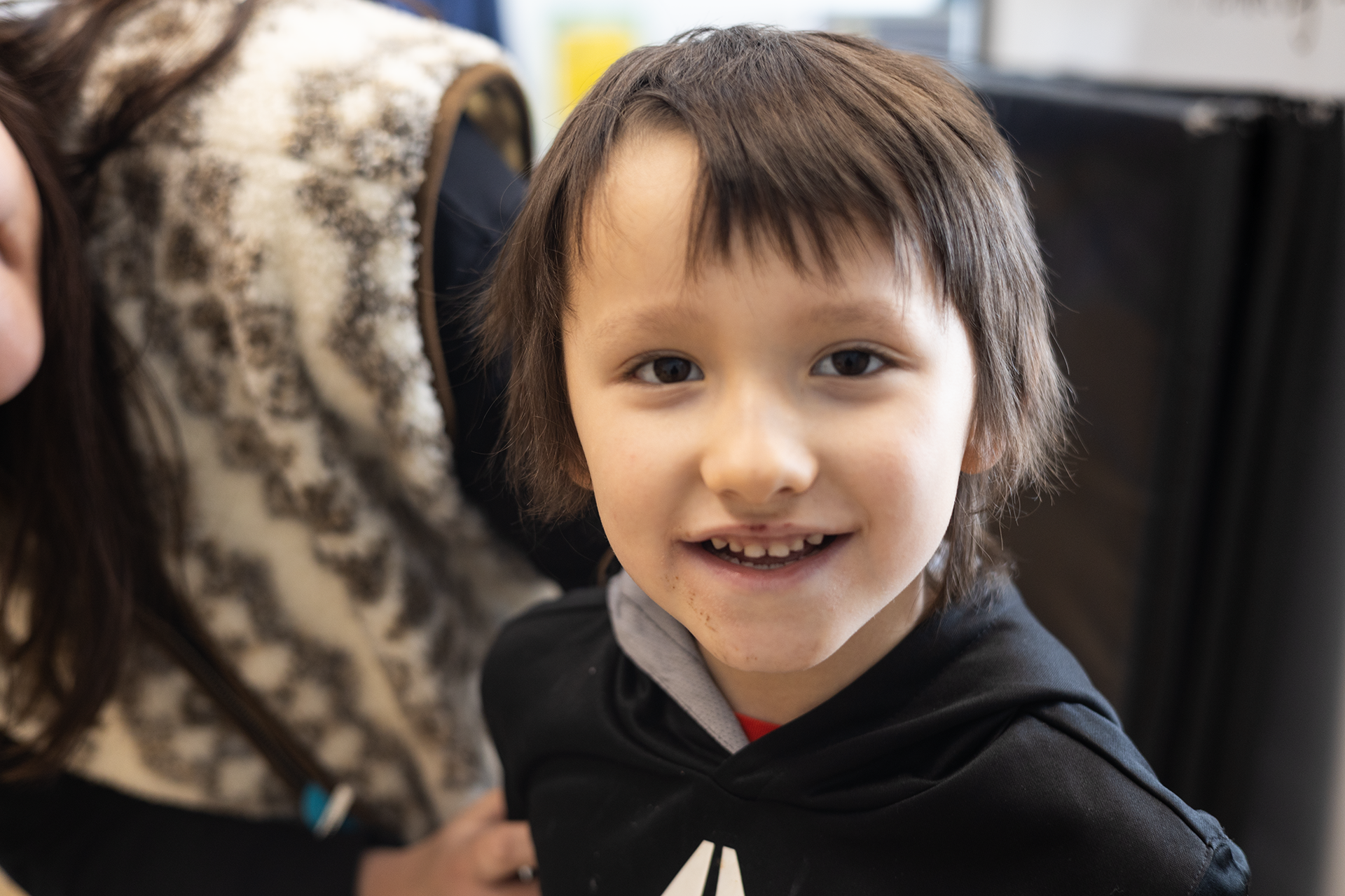 A young boy in a black sweatshirt smiles.