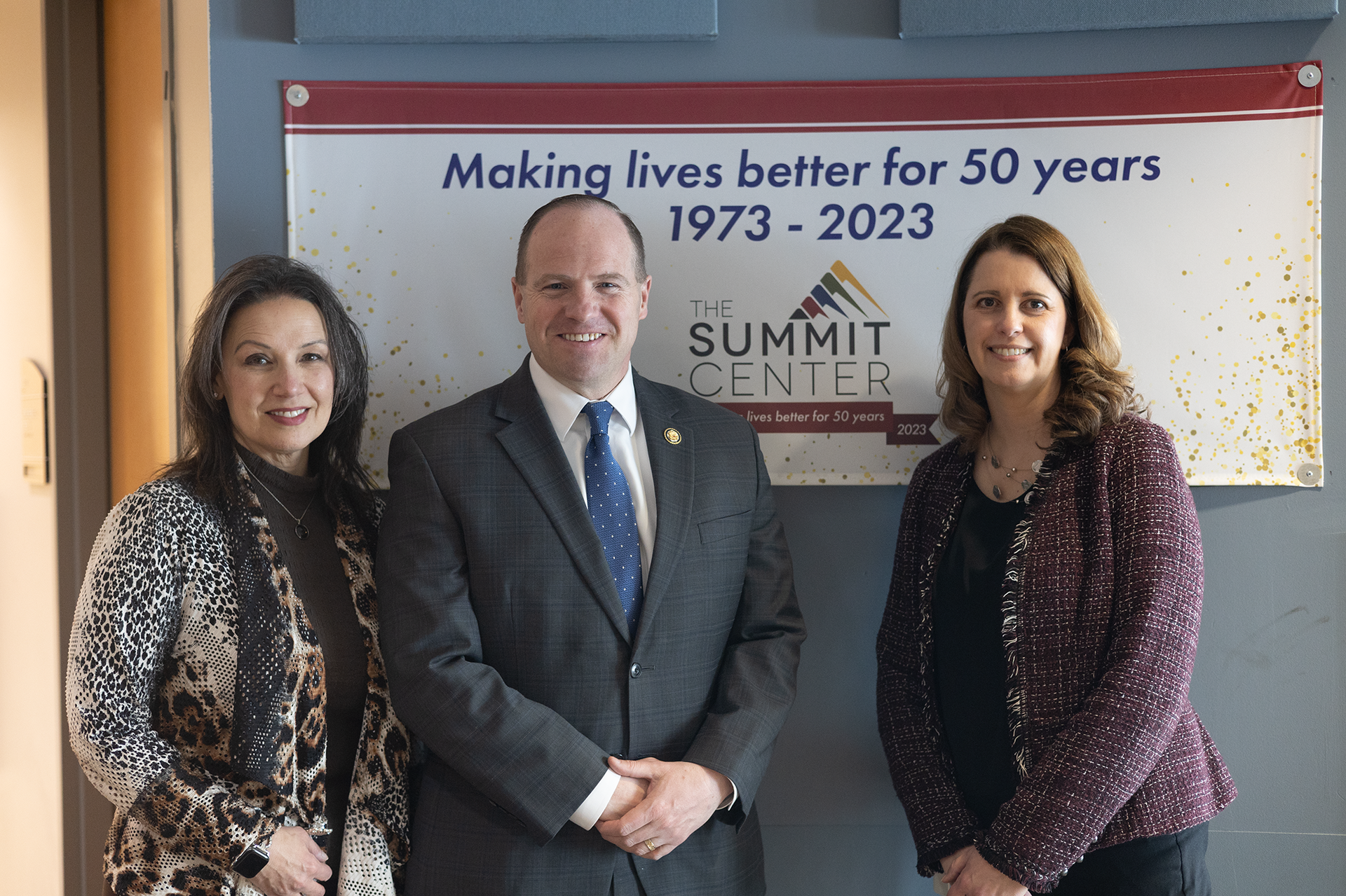 Summit CEO Lisa Foti, Rep. Tim Kennedy, and Summit President Amy Jablonski pose in front of The Summit Center banner.