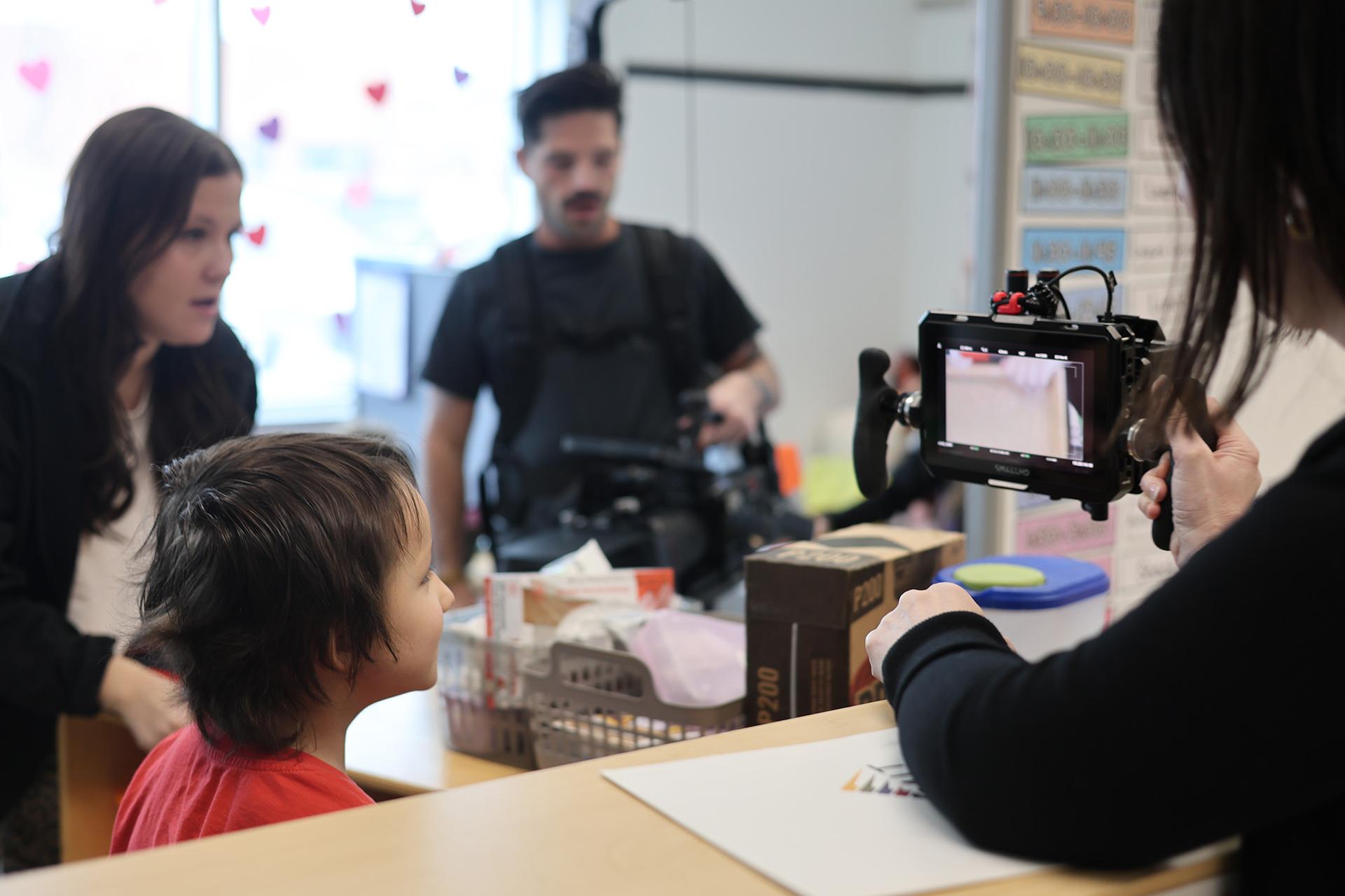 A young boy looks at a film camera in a school classroom.