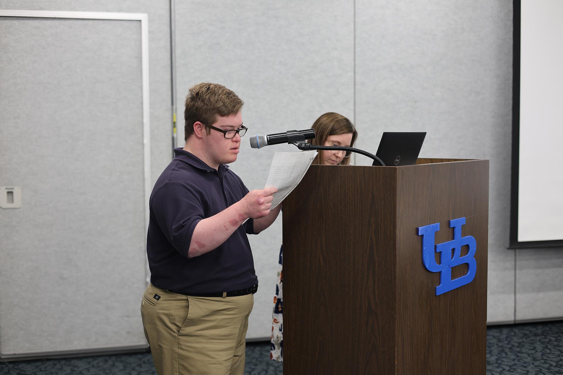 A young man reads from a piece of paper at a podium.