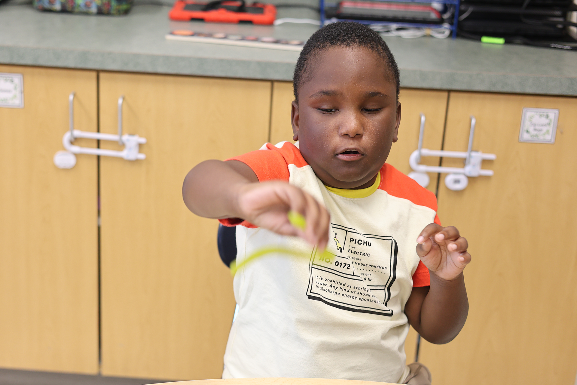 A young boy in a white and orange shirt spins a yellow fidget spinner.