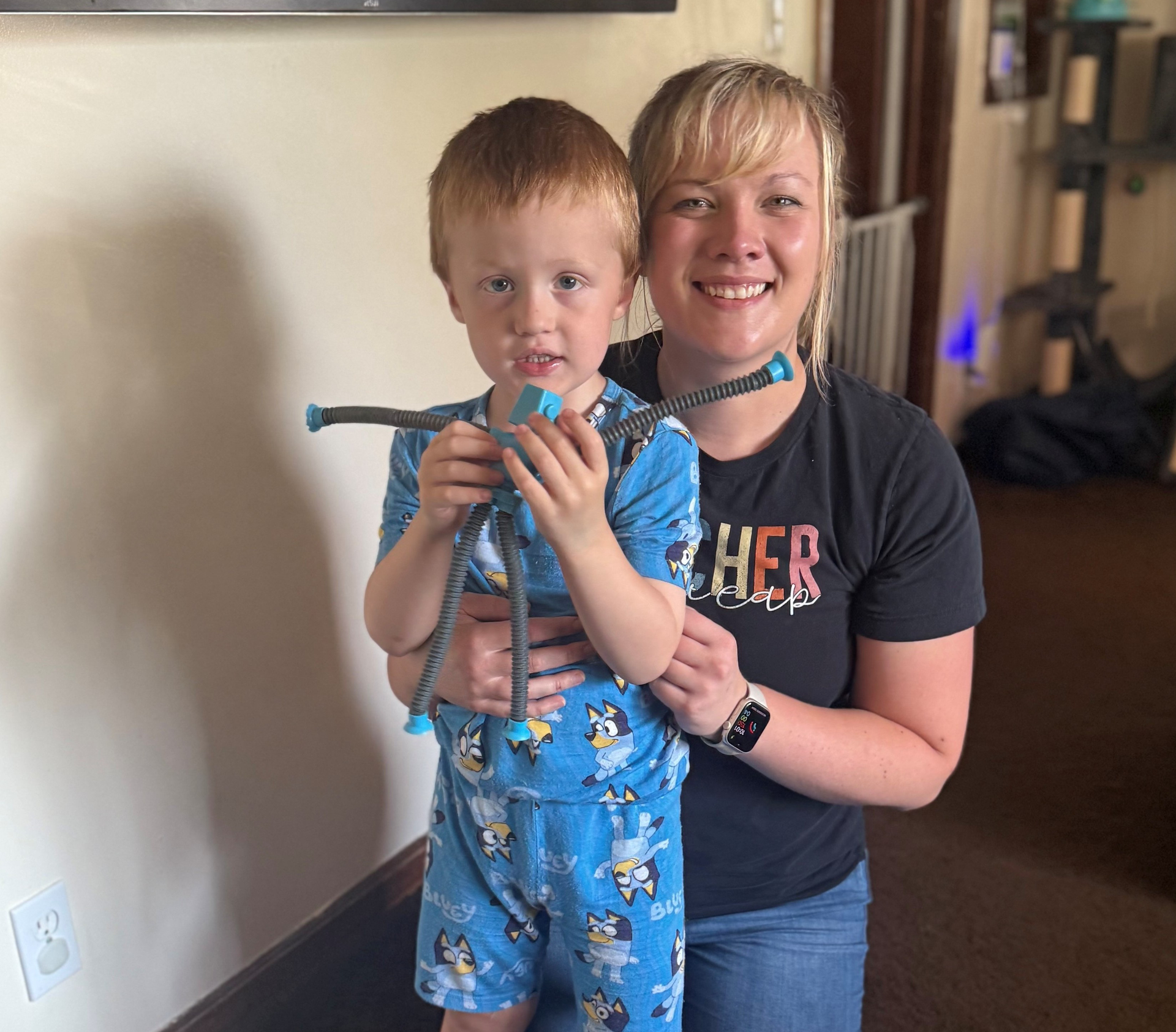 A young boy in blue Paw Patrol pajamas smiles with a young woman in a gray t-shirt and jeans.
