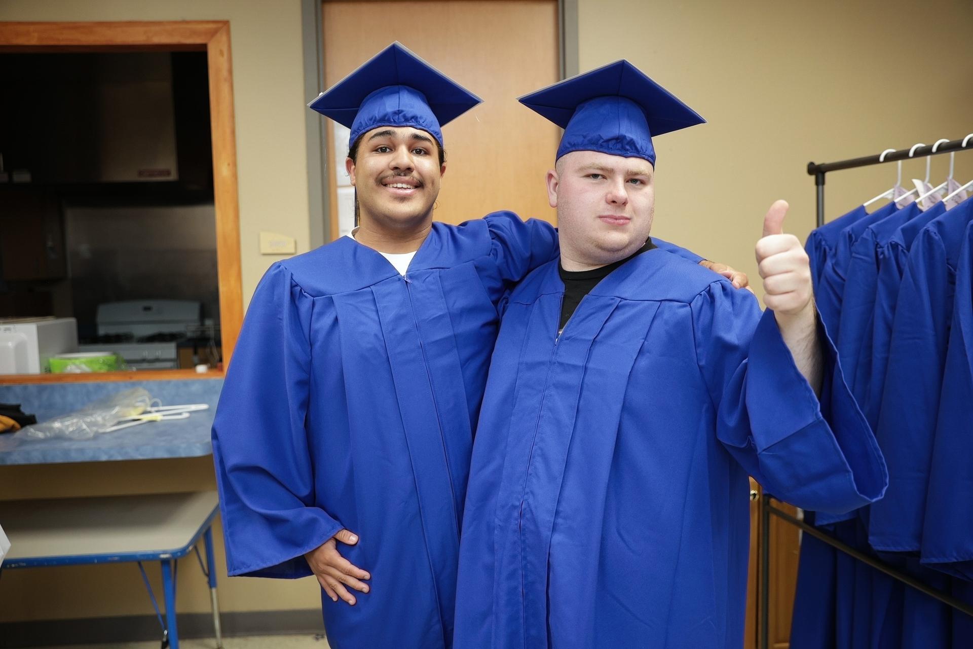 Two young men pose wearing blue graduation caps and gowns.