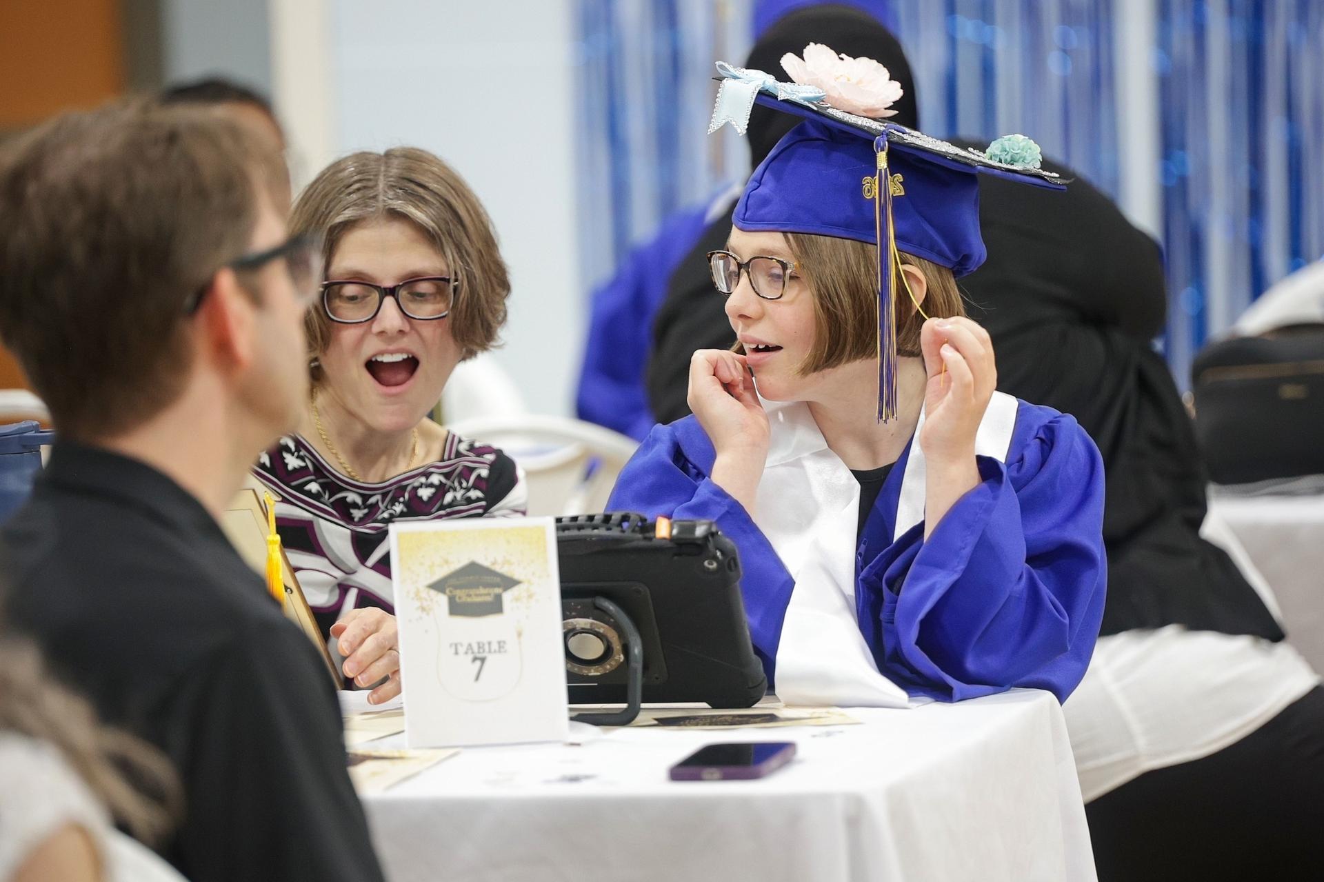 A young woman wearing a blue graduation cap sits with her family.