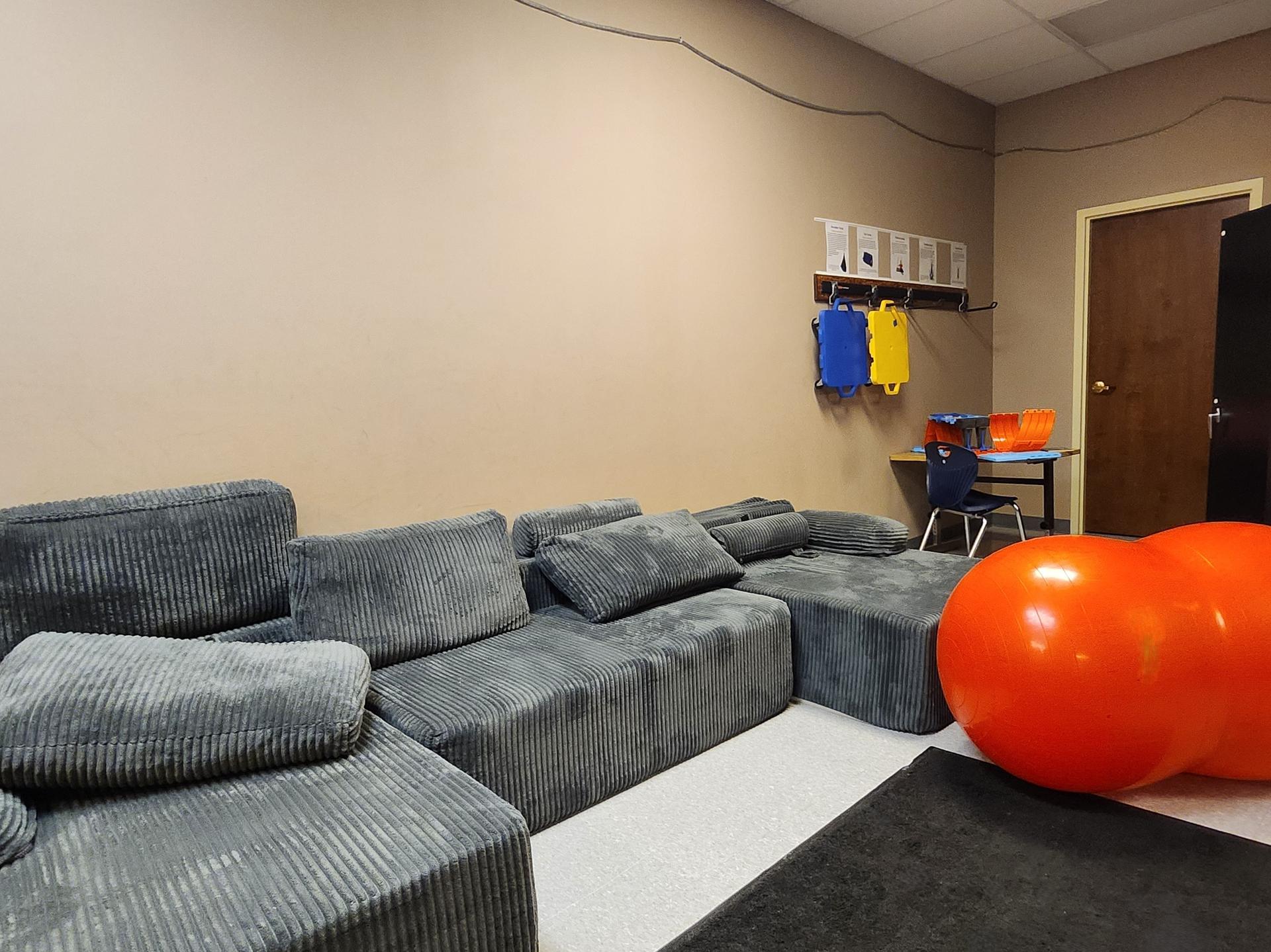 A gray couch with lounge seating, two orange exercise balls in a cream colored room.