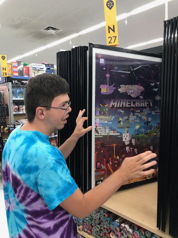 A young man in a tie dye shirt looks through posters at a store.