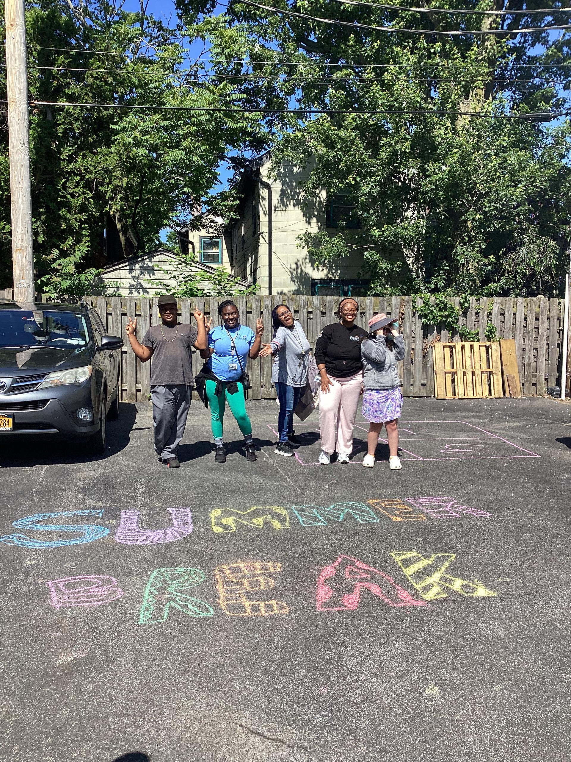 A group of people stand in a parking lot by the words 