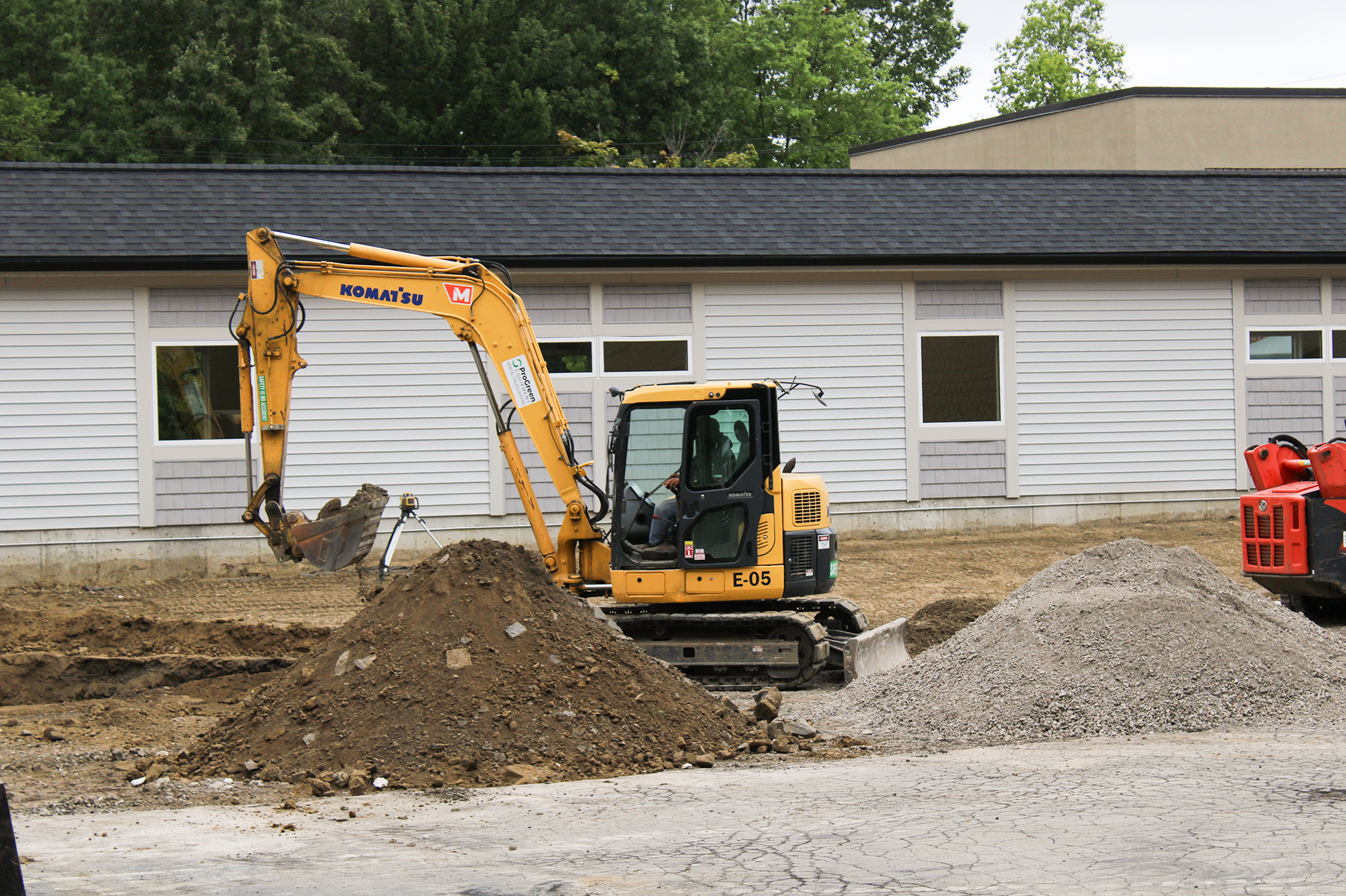 An excavator lifts dirt from a hole outside a white building.