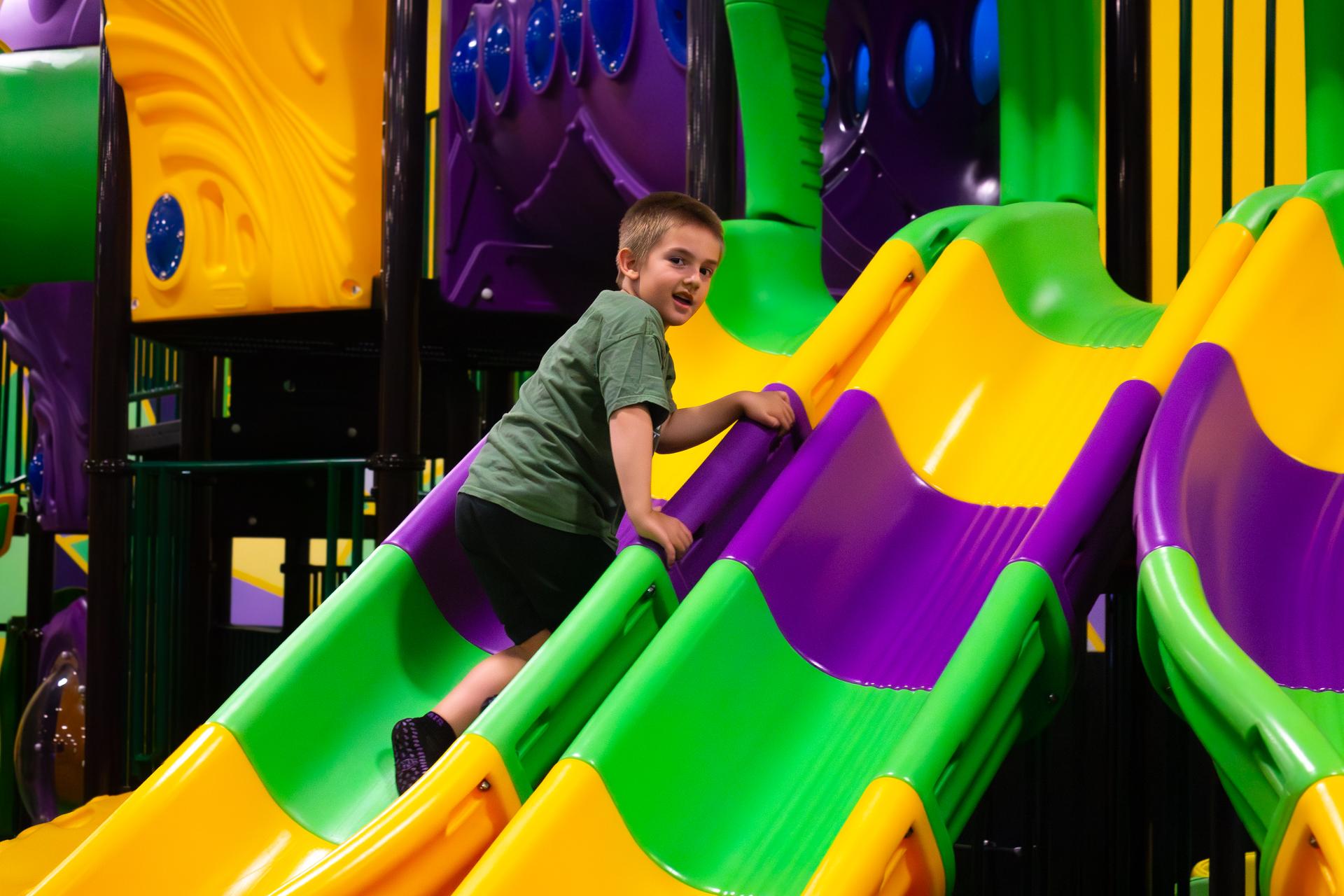 A young boy climbs up a yellow, green, and purple striped slide.
