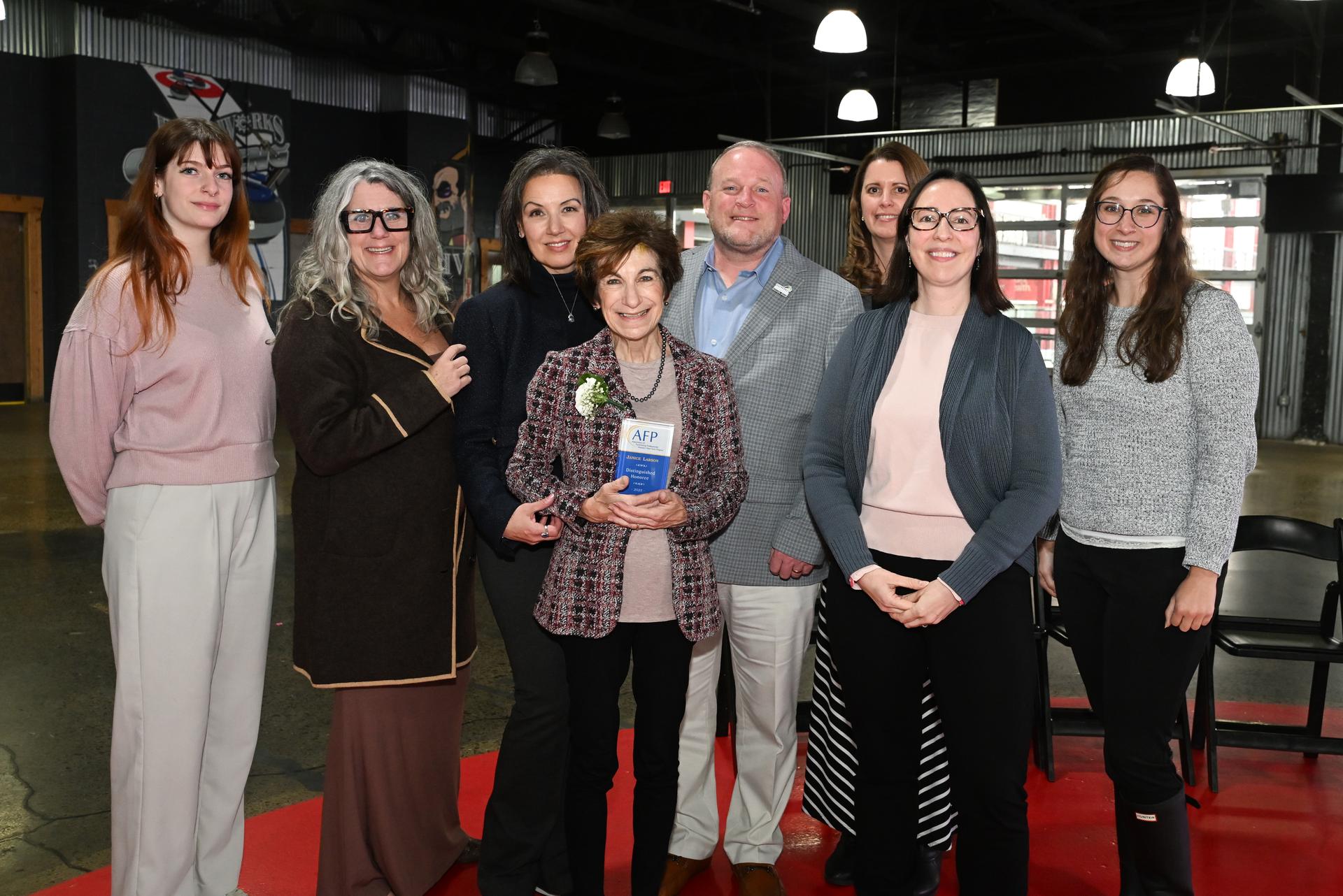 A group of a people in business attire pose with an award at an industrial style room.
