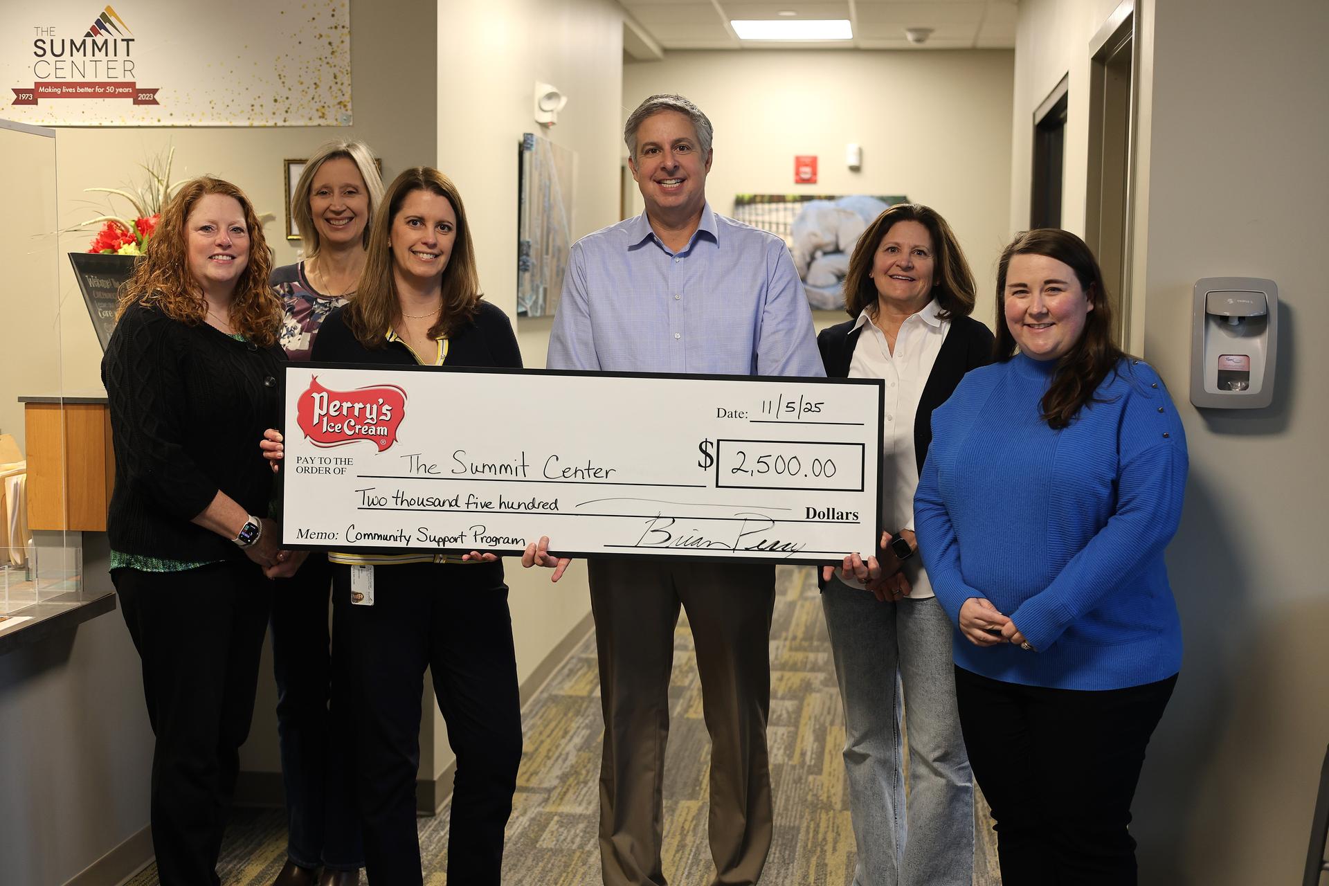 A group of six professionals hold a check with the Perry's logo on it at the Summit Behavioral Pediatrics Clinic.