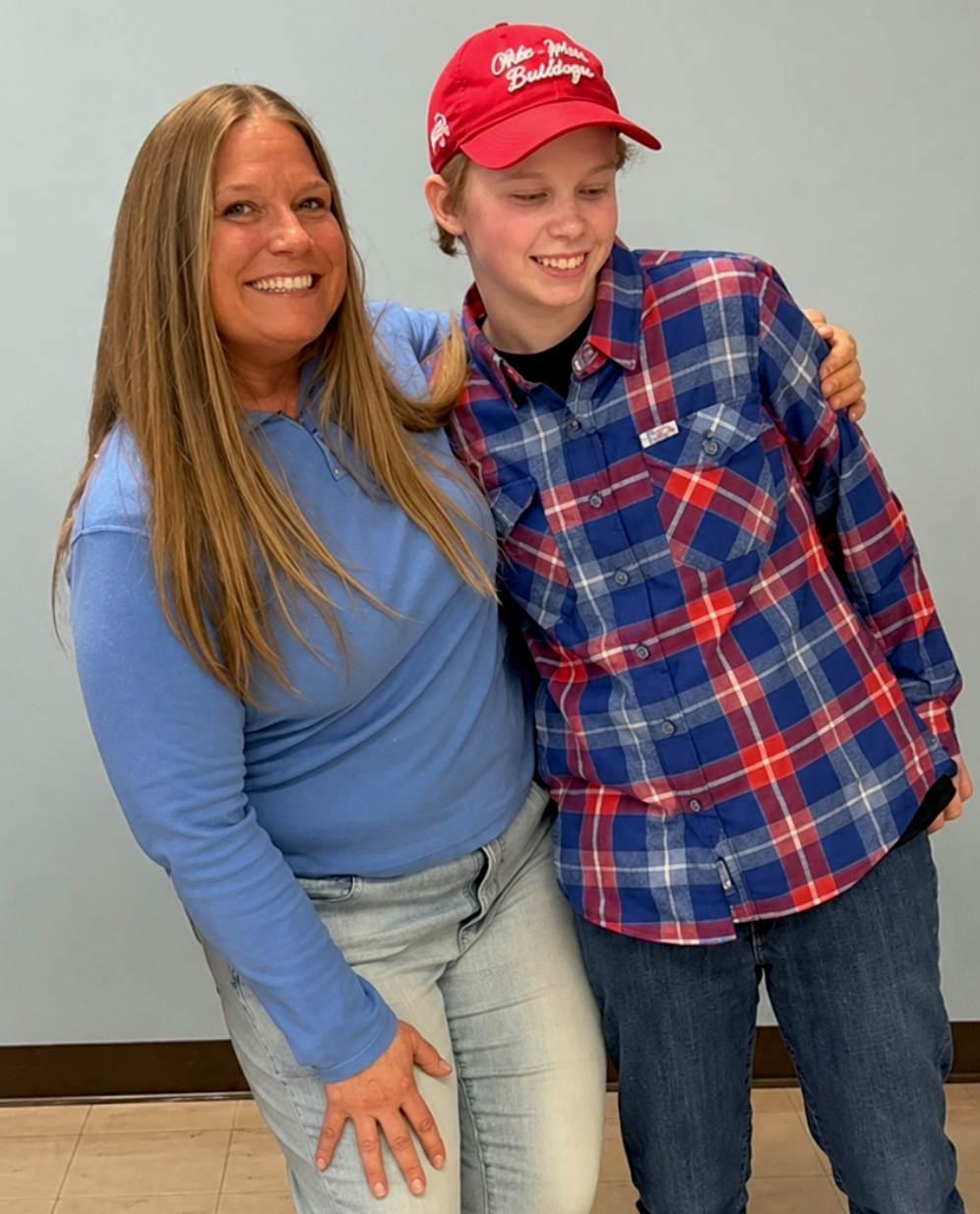 Two women smile and pose in front of a gray wall.
