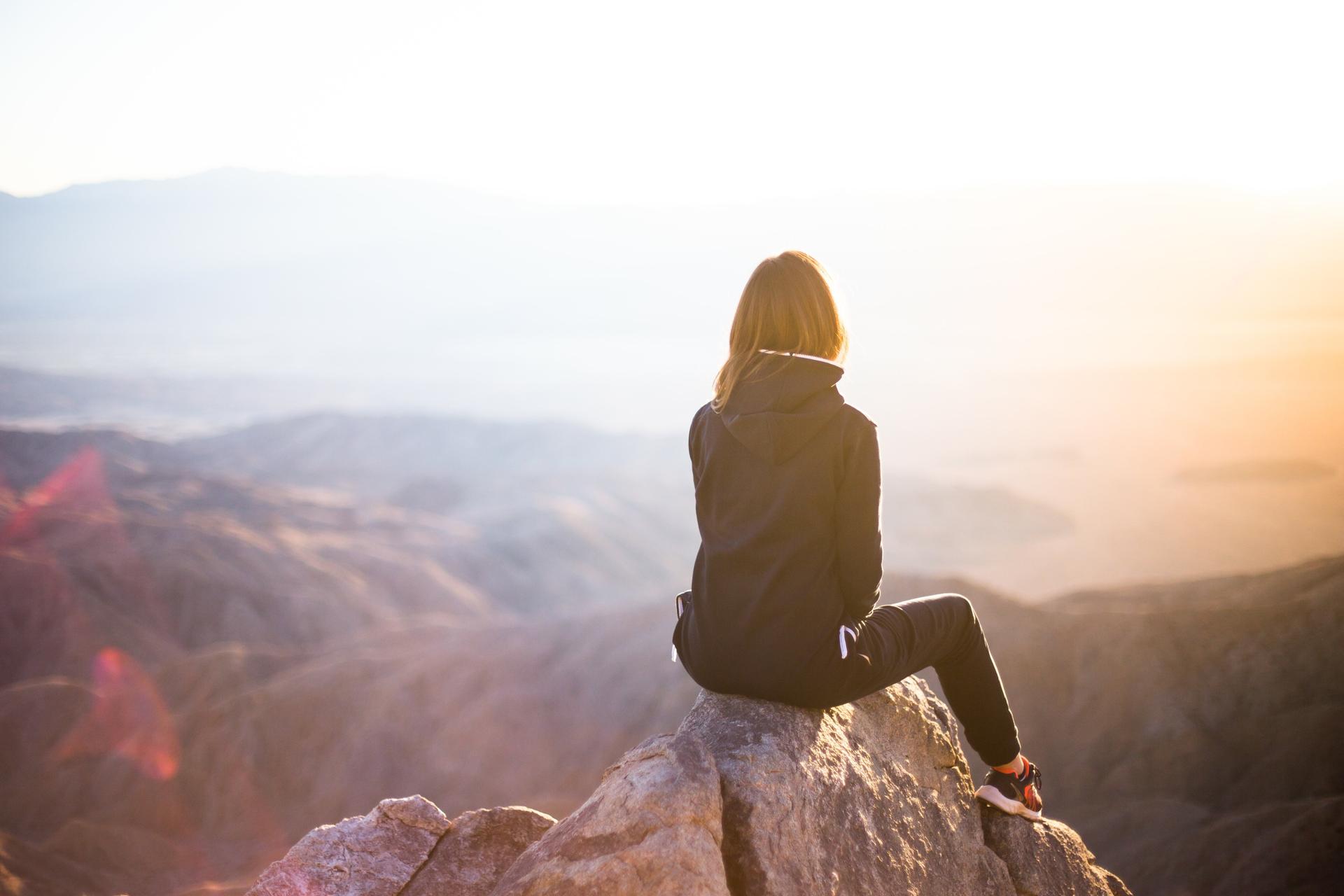 A woman sitting on a mountaintop looking at the view.