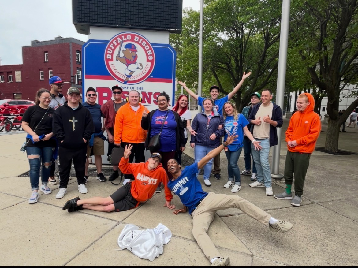 A group of people post outside around a sign for the Buffalo Bisons baseball team.