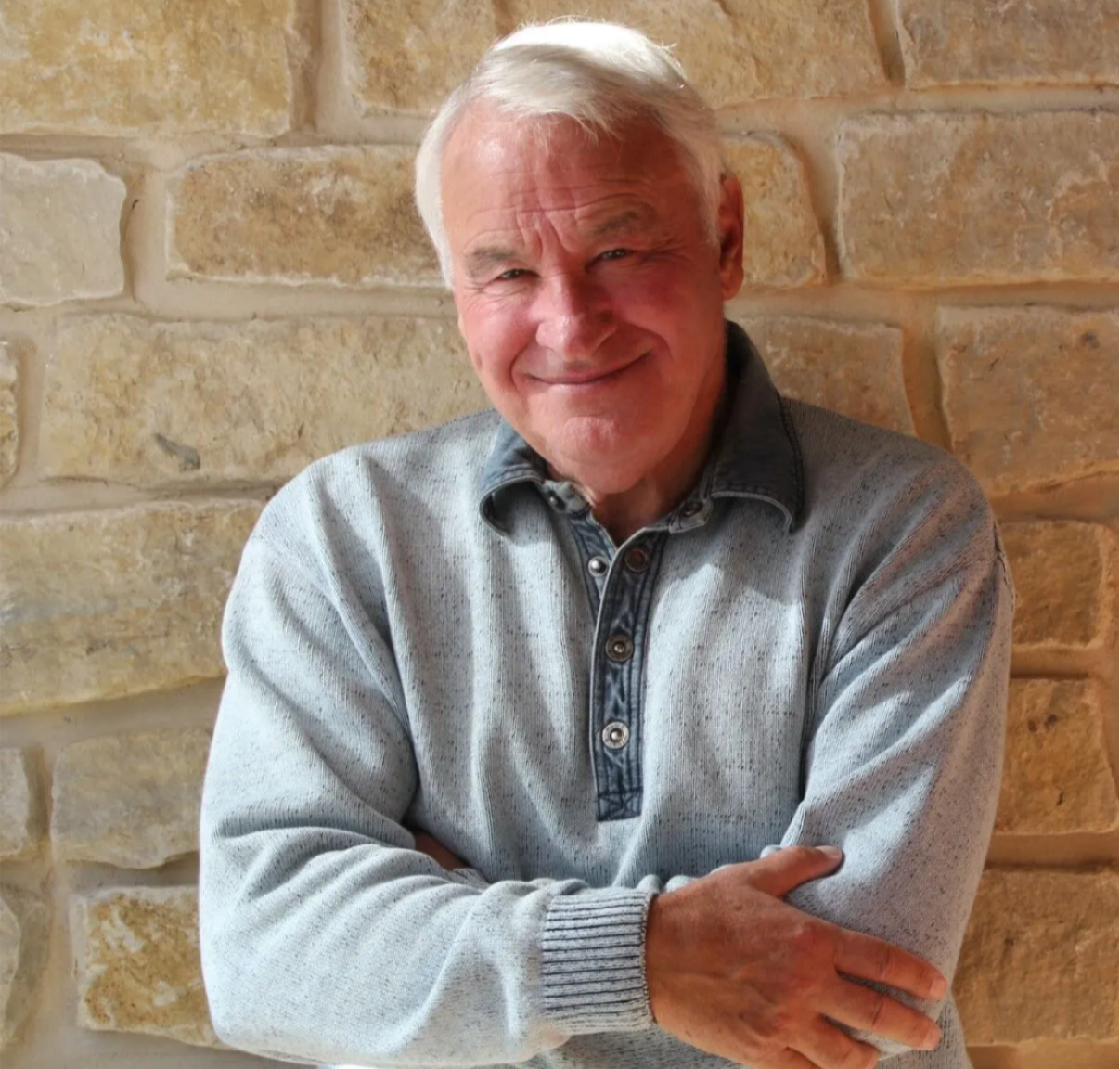 Tom Golisano, founded of Paychex, stands in front of a beige brick background.
