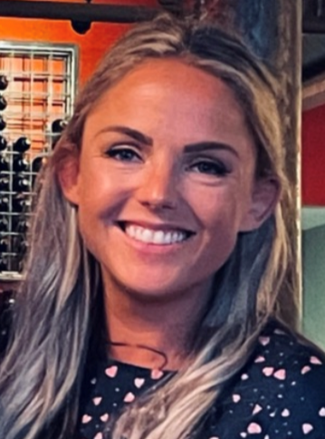 A young woman in a blue top with hearts smiles.