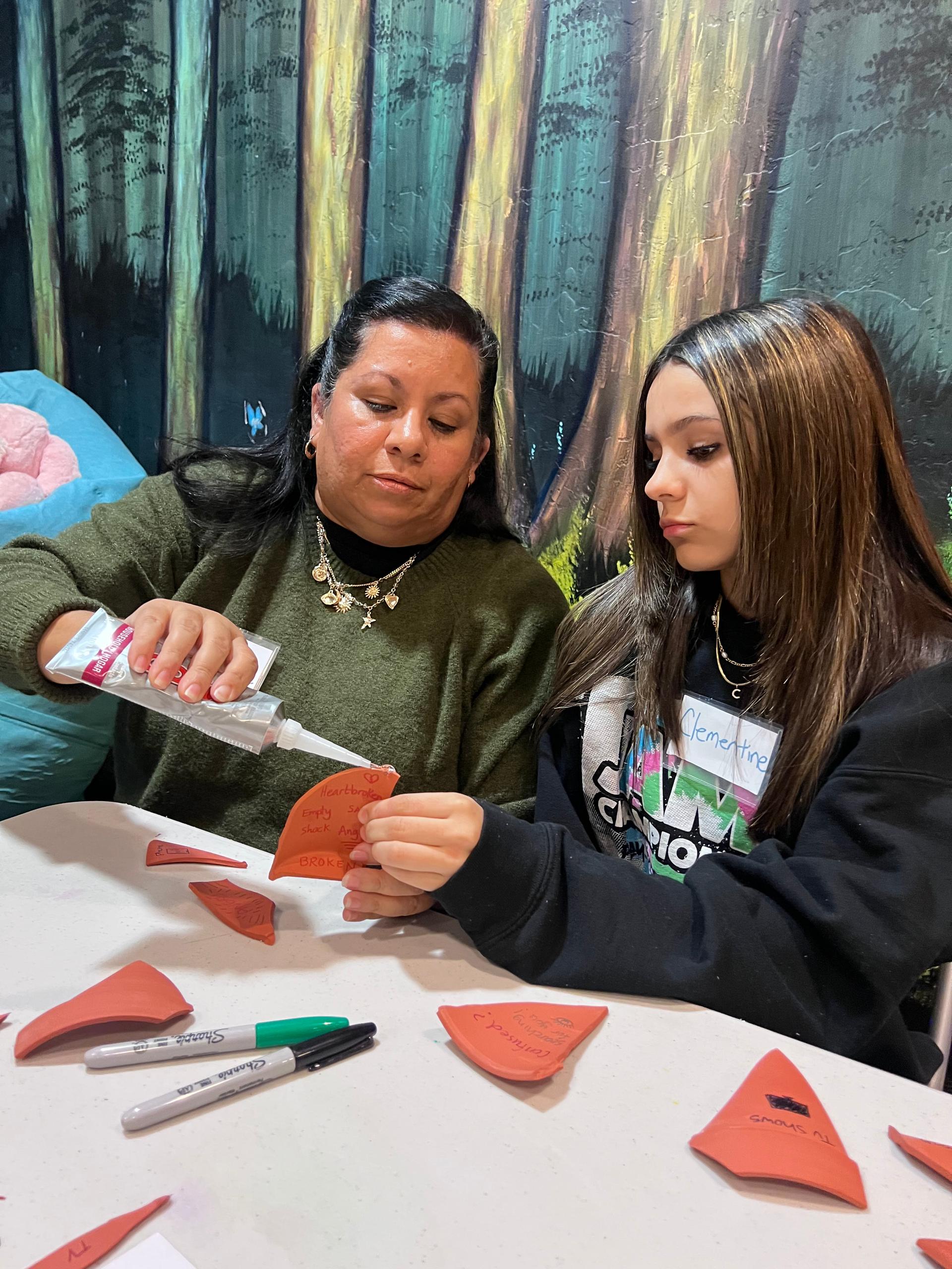 A phot of a caregiver and a child work together to glue pieces of a broken pot back together. A phot of a caregiver and a child work together to glue pieces of a broken pot back together.